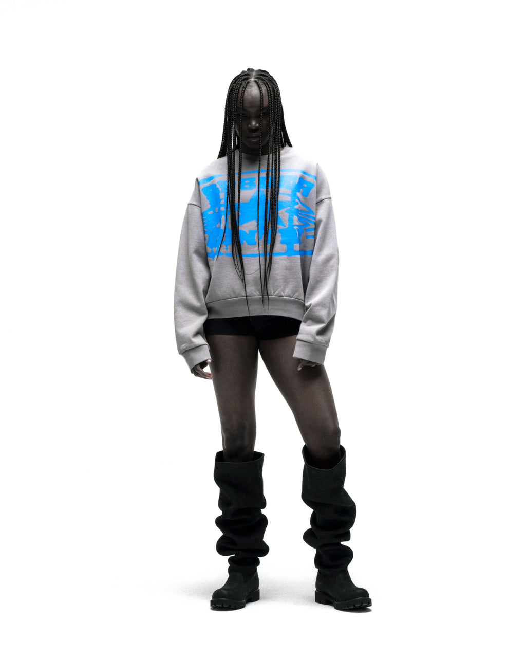Model wearing a grey SP5DER CUNTRY CREWNECK with blue graphic print, black shorts, and tall black boots.