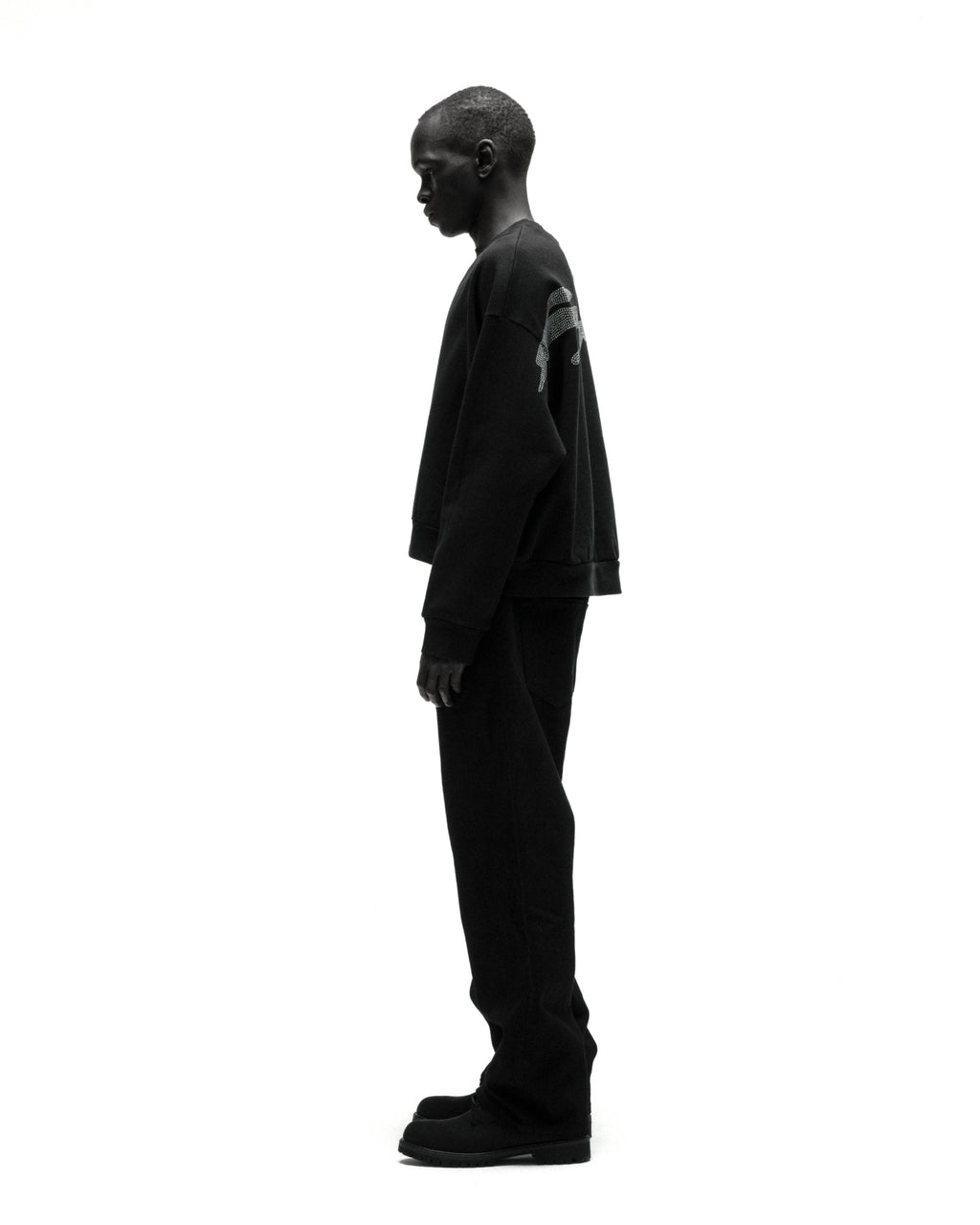 Black cotton fleece crewneck with rhinestone graphic, worn by a model in profile.