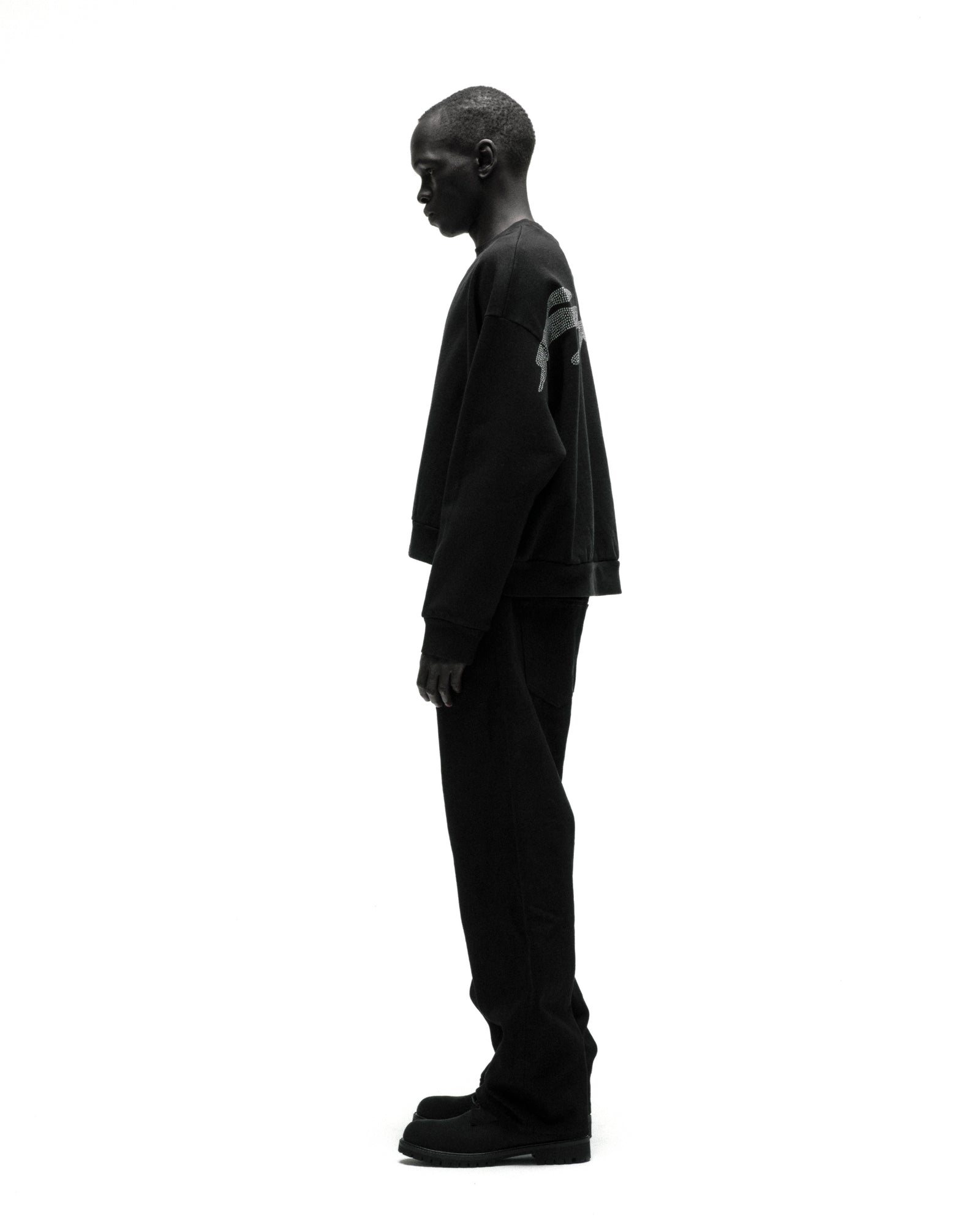 Black cotton fleece crewneck with rhinestone graphic, worn by a model in profile.