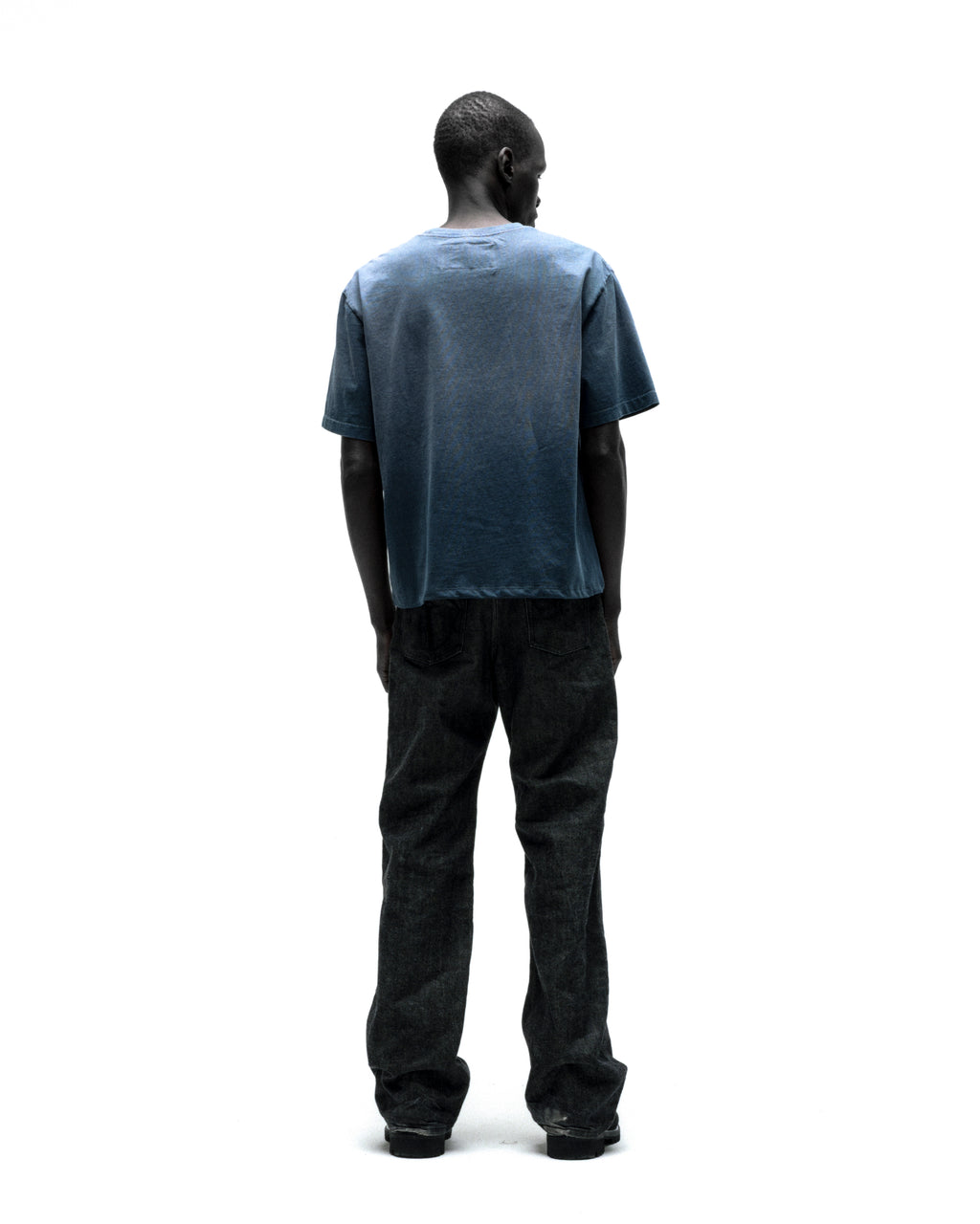 Man from behind wearing a faded blue cotton SP5DER CUNTRY TEE with a graphic print and dark jeans.