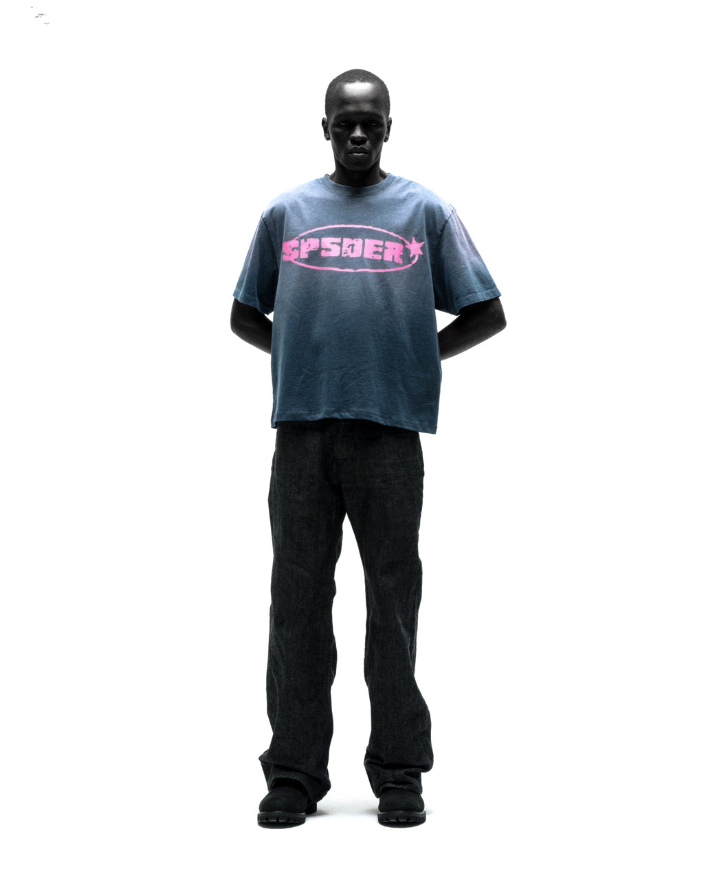 Man in faded blue cotton FORM 5 TEE with pink "SP5DER" graphic and dark jeans.