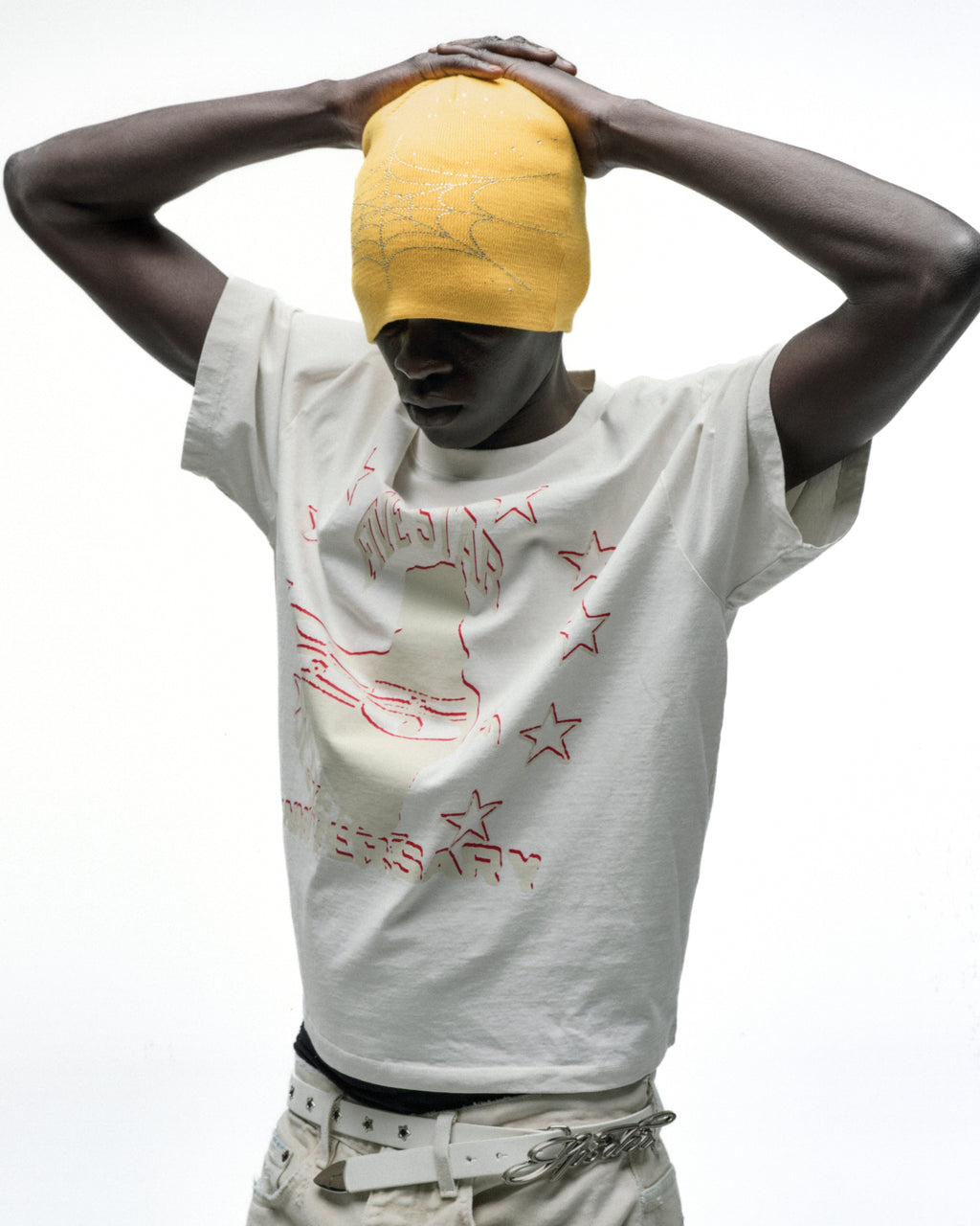 Model in a white cotton ANNIVERSARY TEE with red graphic print and a yellow beanie.