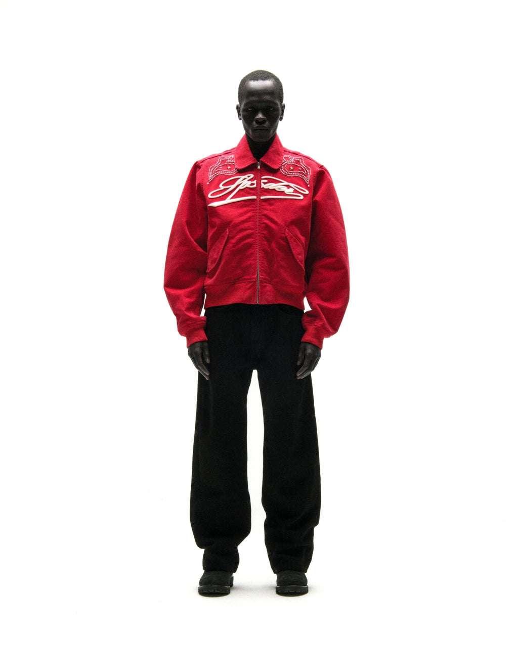 Red cotton canvas bomber jacket with white embroidered script and studded shoulders.