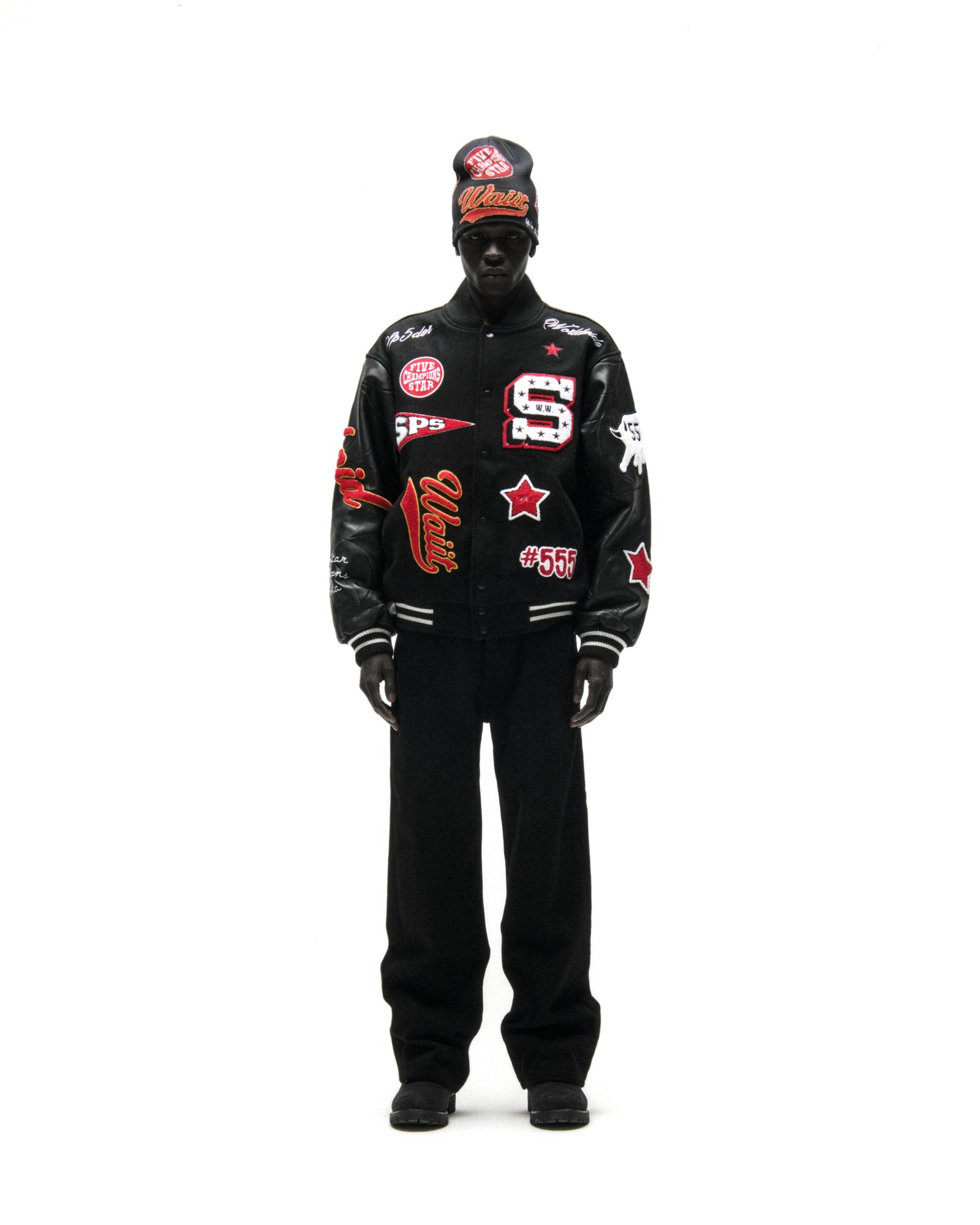 Black wool varsity jacket with leather sleeves, debossed web design, and multiple embroidered patches.