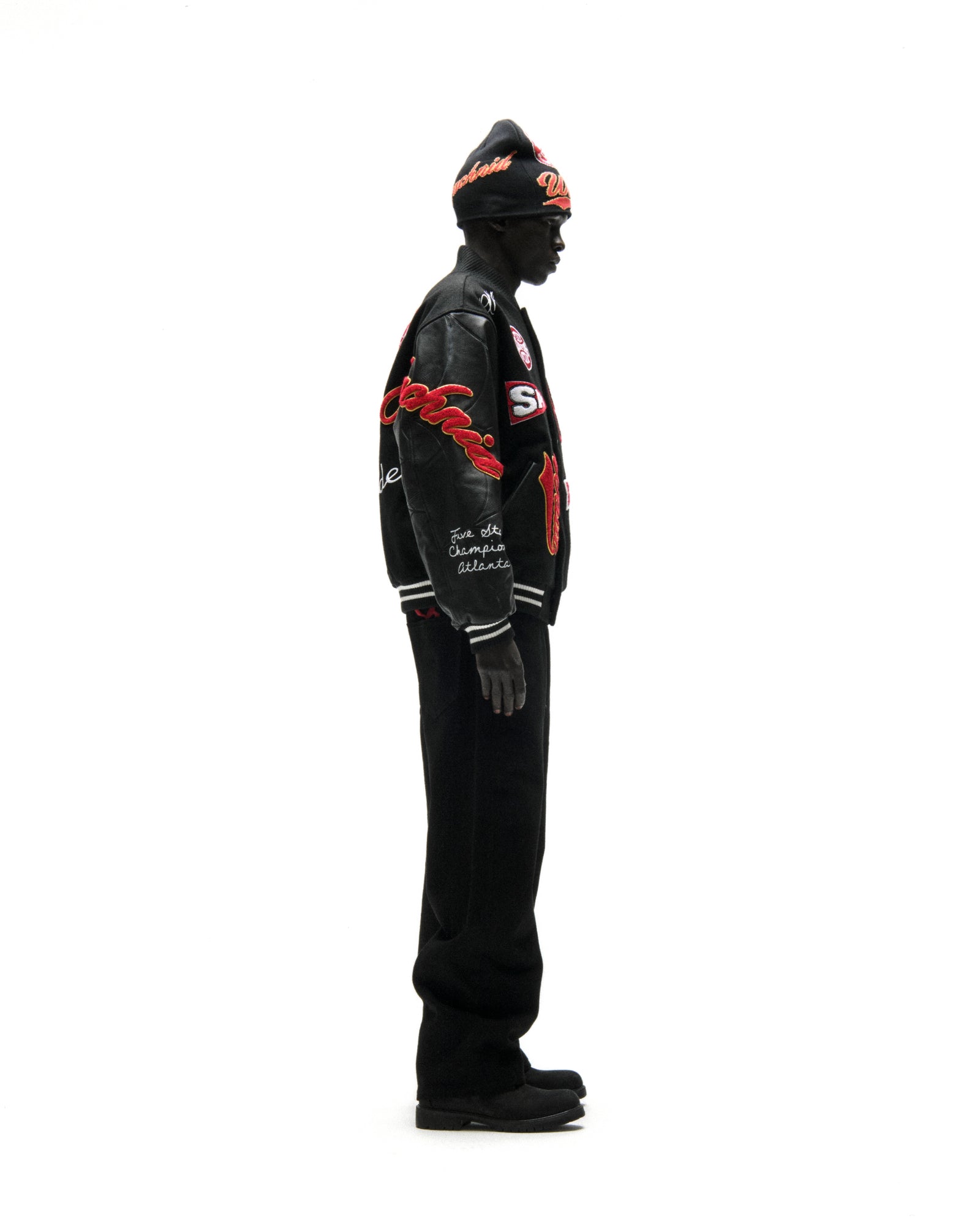 Black wool varsity jacket with leather sleeves, debossed web design, and red embroidered patches.