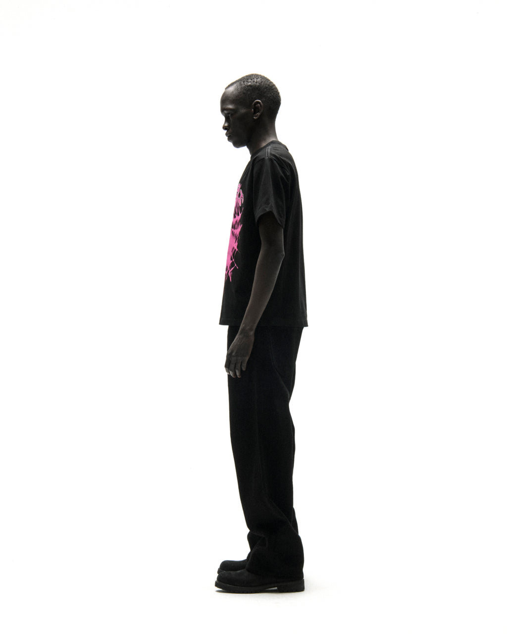 Black cotton tee with "SP5DER" text in pink rhinestones on front, worn by a man in profile.