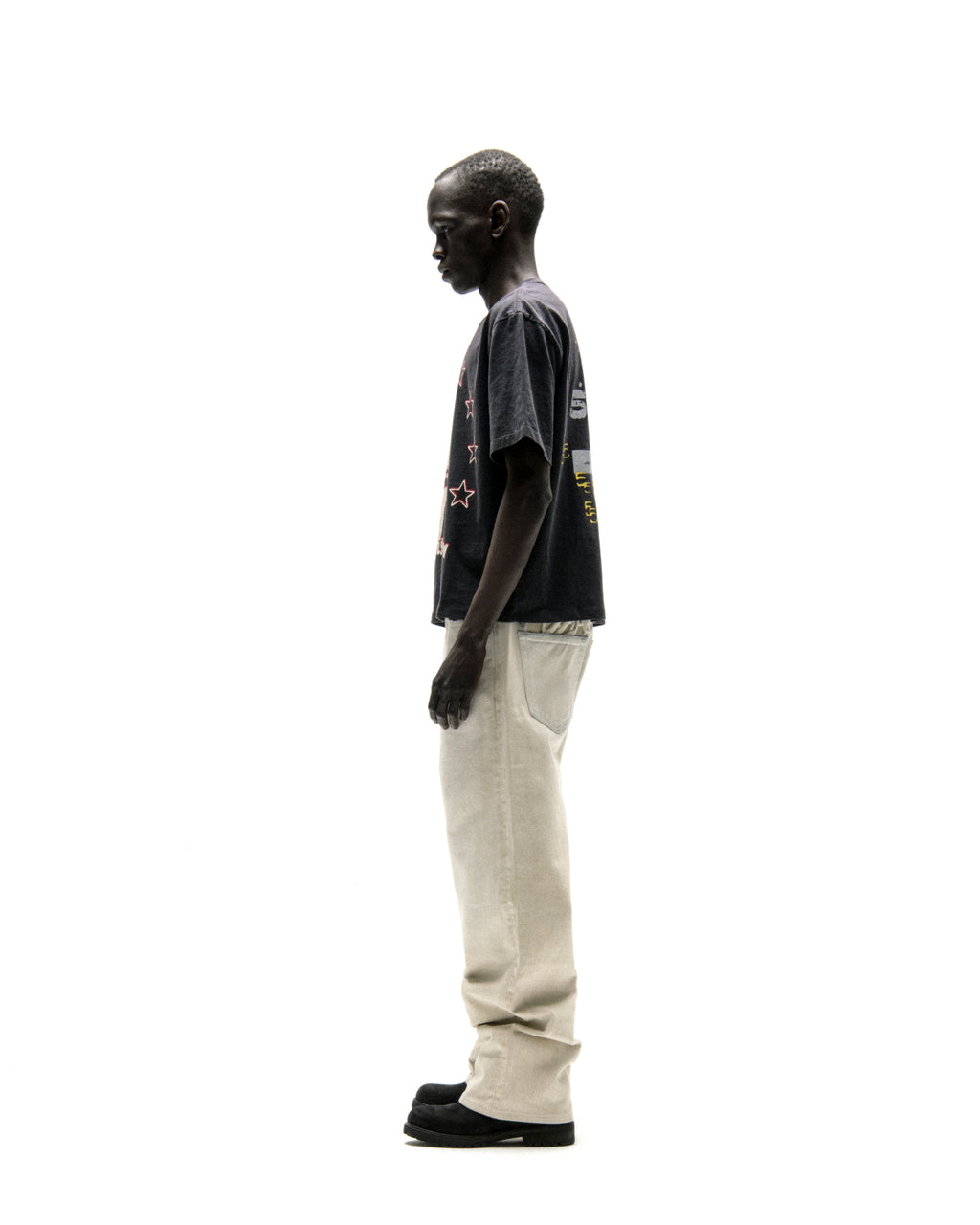 Man in black cotton Anniversary Tee with graphic print and light beige pants.