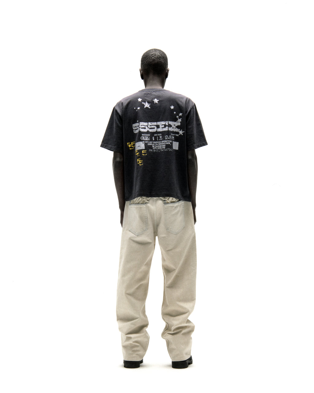 Man in black cotton ANNIVERSARY TEE with "ESSEX" graphic and stars, paired with light beige pants.