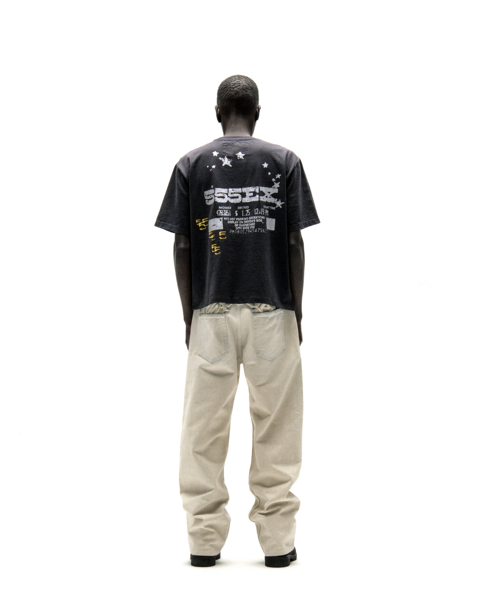 Man in black cotton ANNIVERSARY TEE with "ESSEX" graphic and stars, paired with light beige pants.