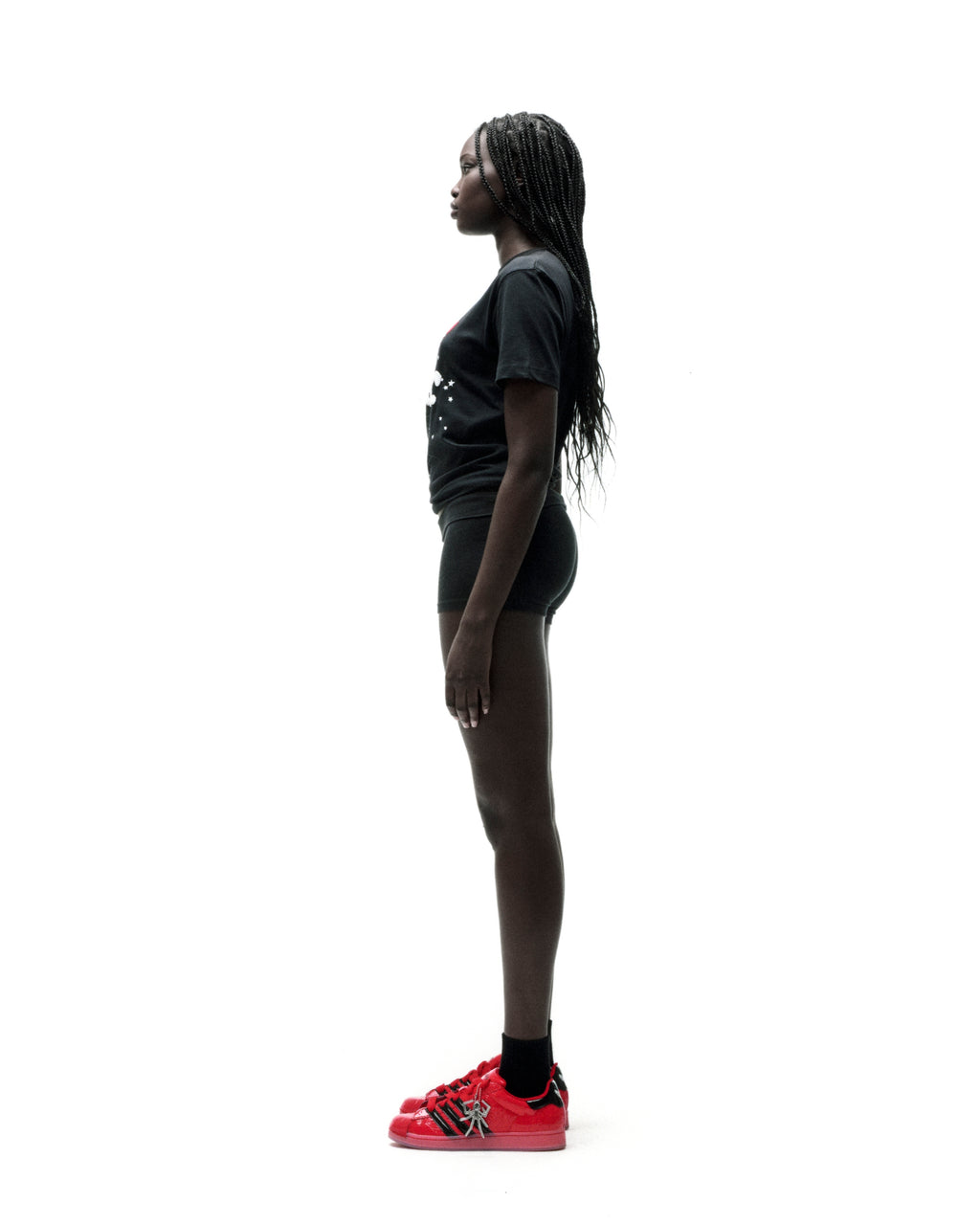 Black Adidas Souvenir Tee with Trefoil x SP5DER graphic, worn by a model in black shorts and red shoes.