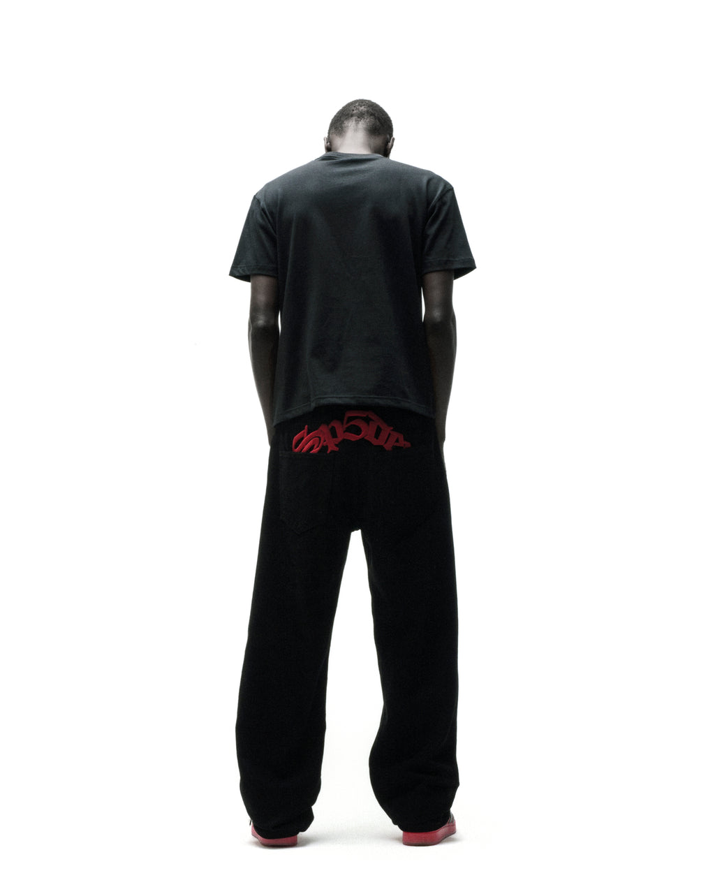 Man in black t-shirt and black pants with red "SP5DER" graphic on the back.