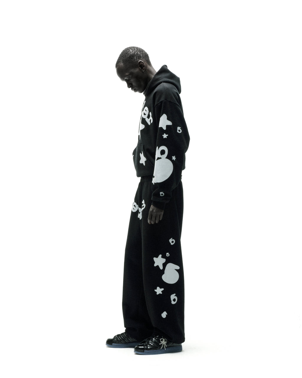 Black cotton fleece hoodie and sweatpants with reflective white 'SP5DER' and star print.