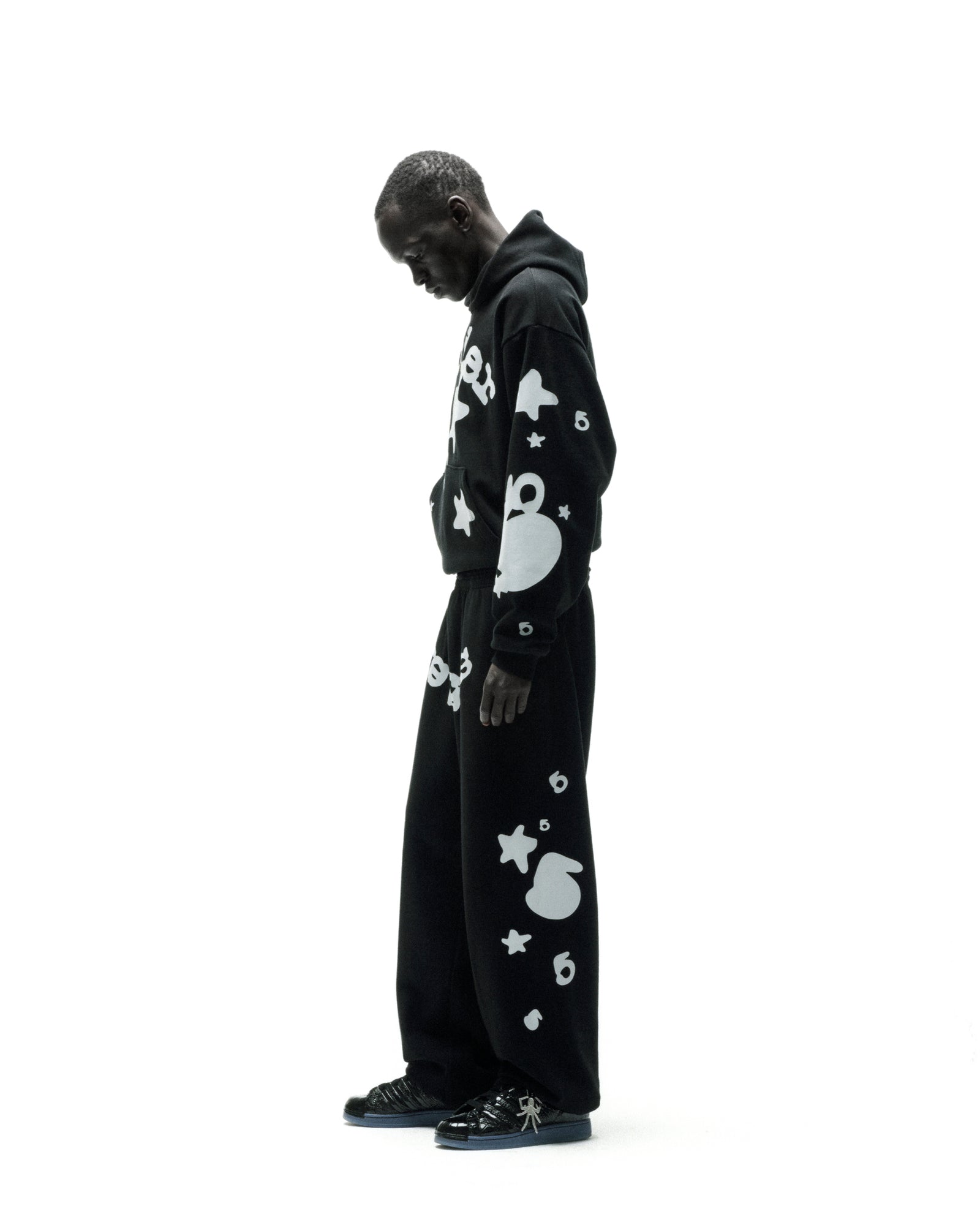 Black cotton fleece hoodie and sweatpants with reflective white 'SP5DER' and star print.