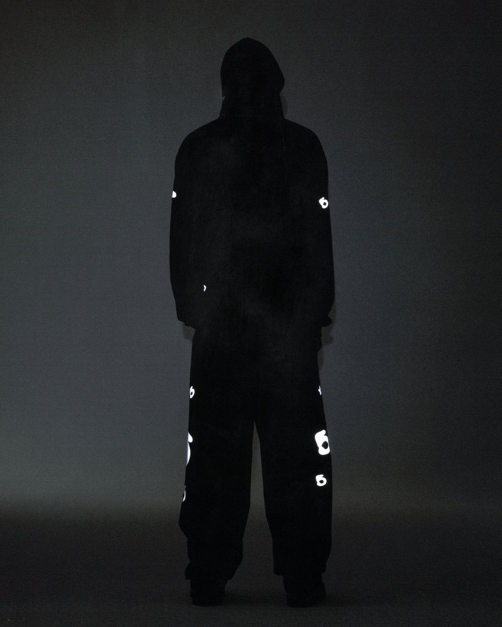 Dark figure wearing a black reflective Beluga hoodie and matching pants with 'SP5DER' and star prints.