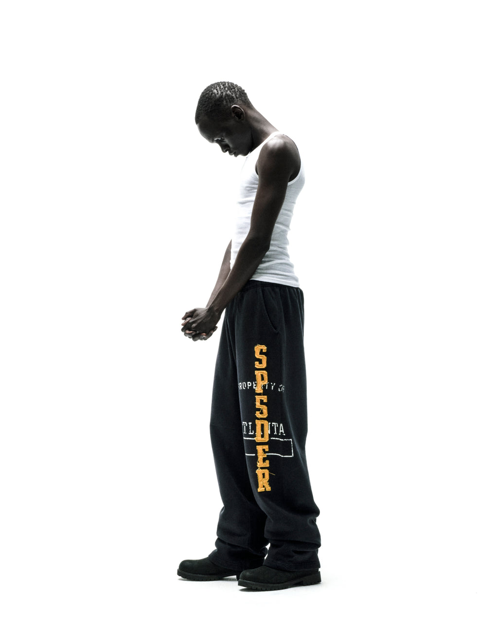 Man in ISSUE 404 black cotton fleece sweatpants with raised chenille "SPSDER" lettering.