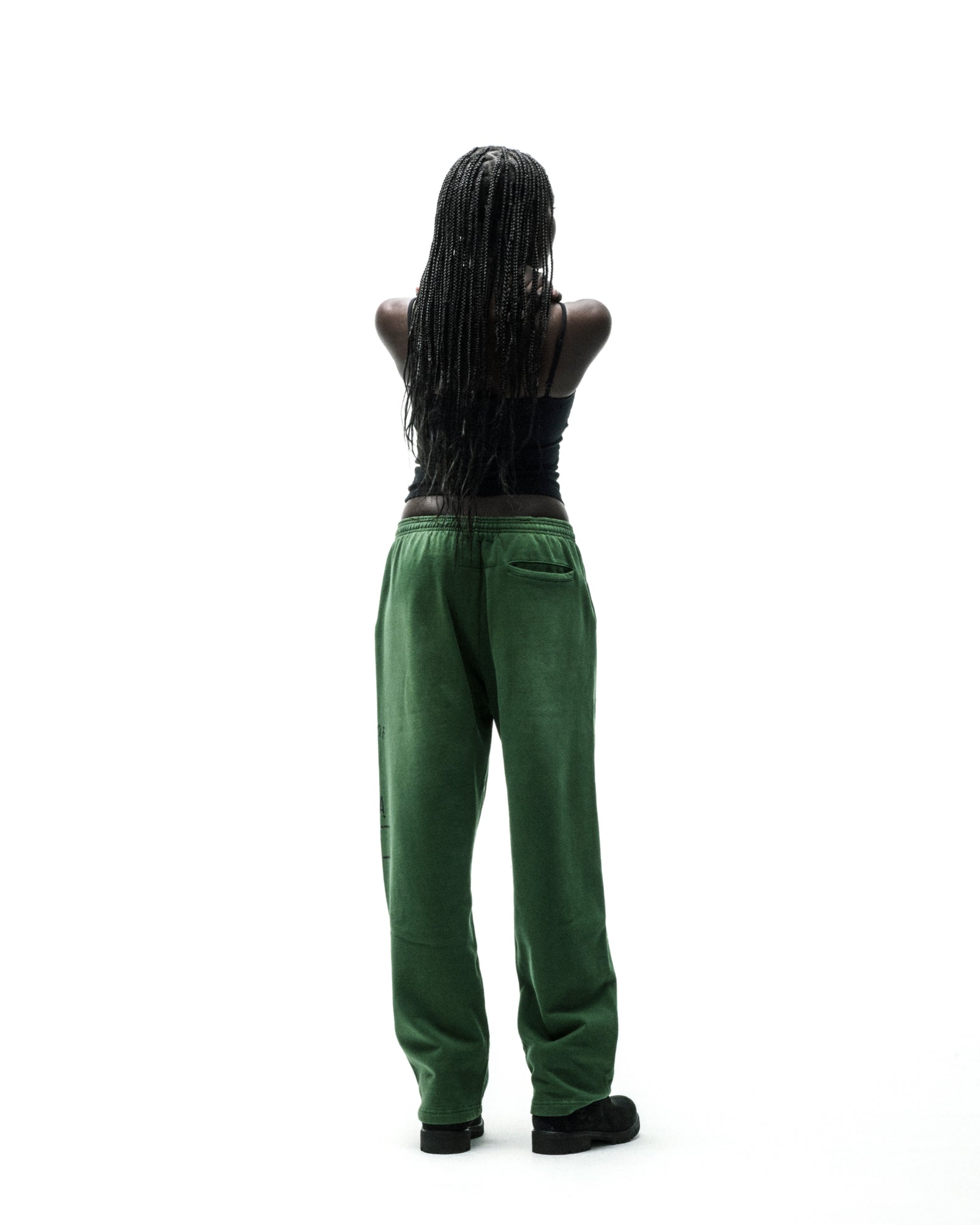 Model from behind wearing wide-leg green fleece sweatpants with faded graphic print and frayed lettering.