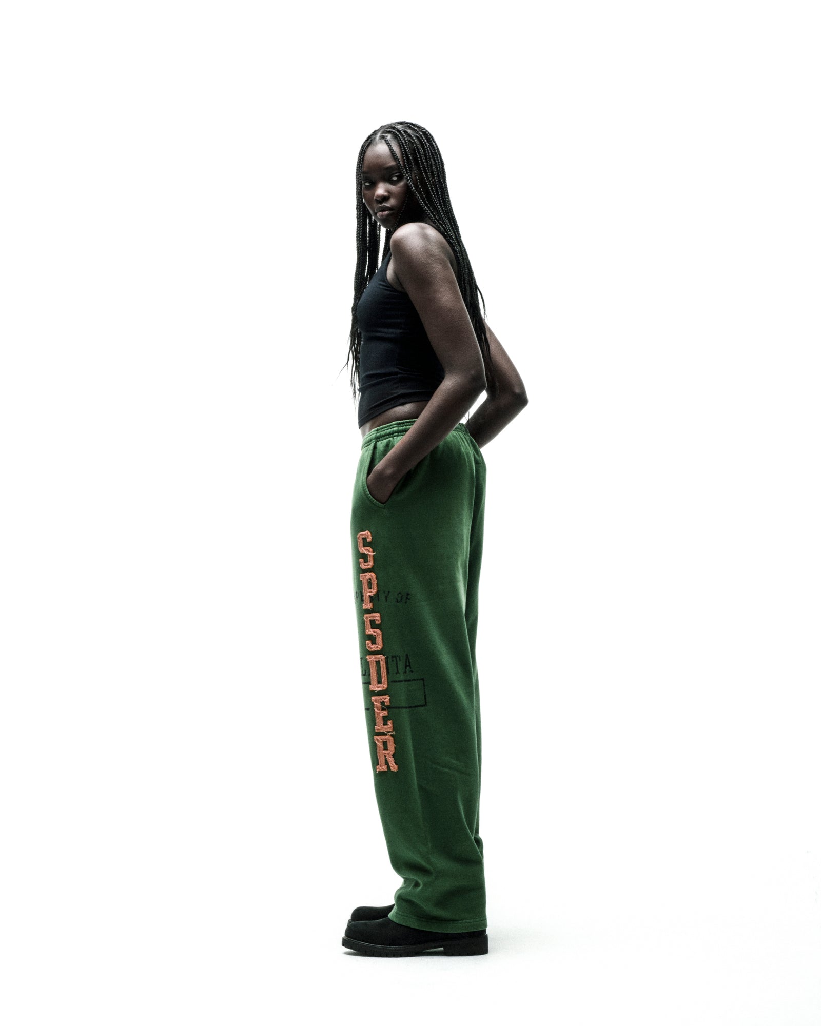 Model wearing green ISSUE 404 wide-leg sweatpants with raised orange "SP5DER" lettering and frayed edges.