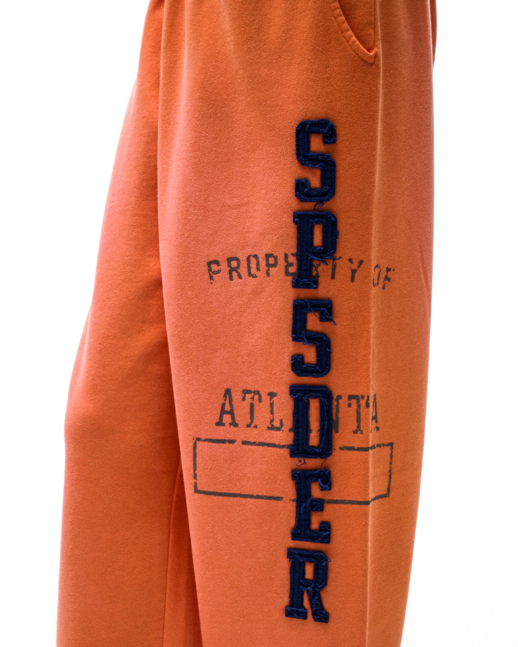 Orange cotton fleece sweatpants with raised, frayed chenille "SP5DER" lettering and faded graphic print.