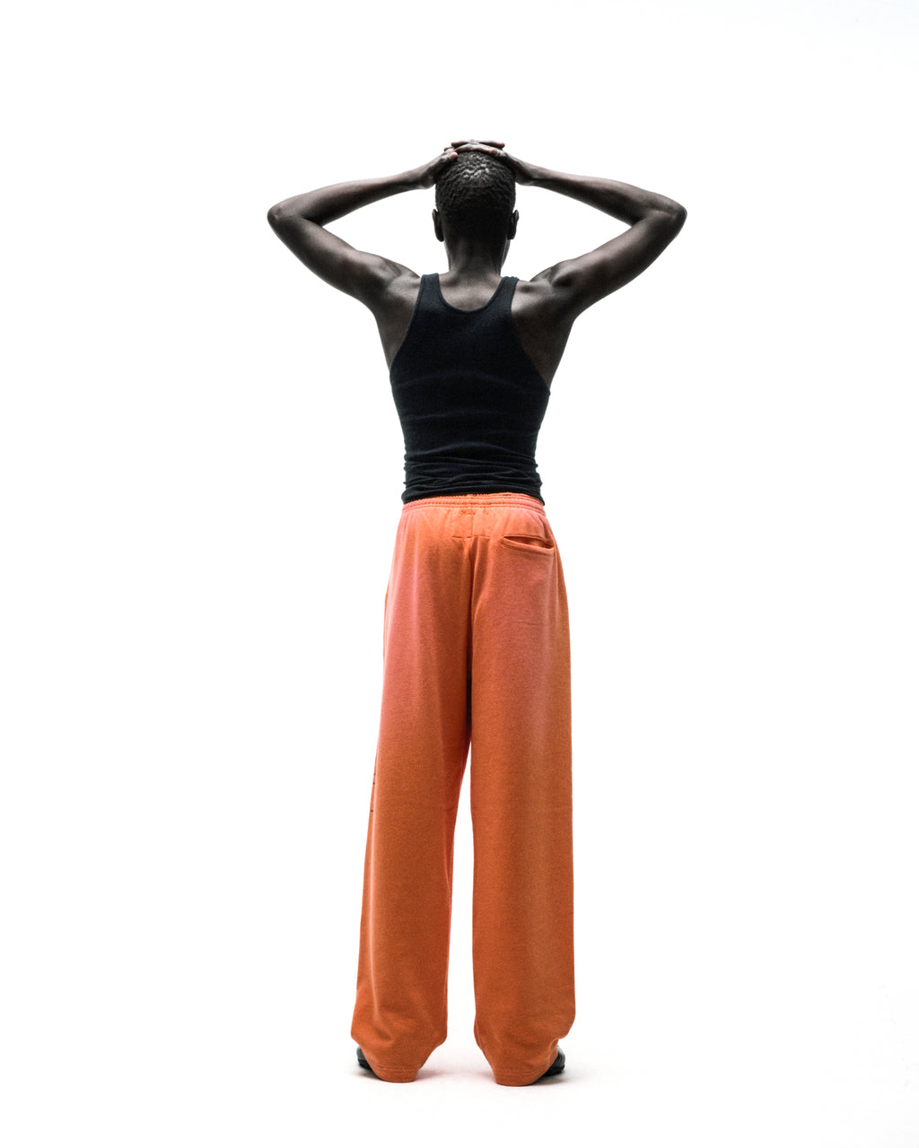 Model from behind wearing wide-leg orange fleece sweatpants with elastic waistband.