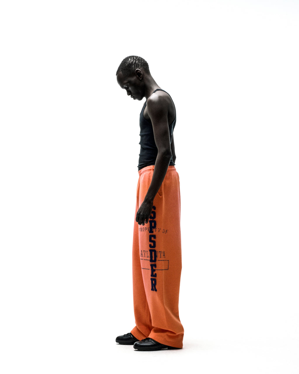 Man in orange ISSUE 404 wide-leg sweatpants with raised chenille "SPSDER" lettering and frayed edges.