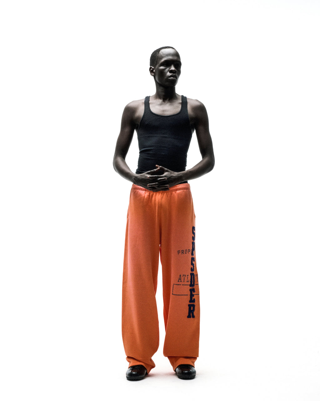 Model wearing orange ISSUE 404 wide-leg sweatpants with faded blue "SPSDER" lettering and frayed edges.