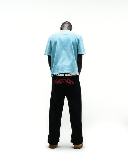 Man from behind wearing a light blue cotton tee and black pants with red embroidered text.