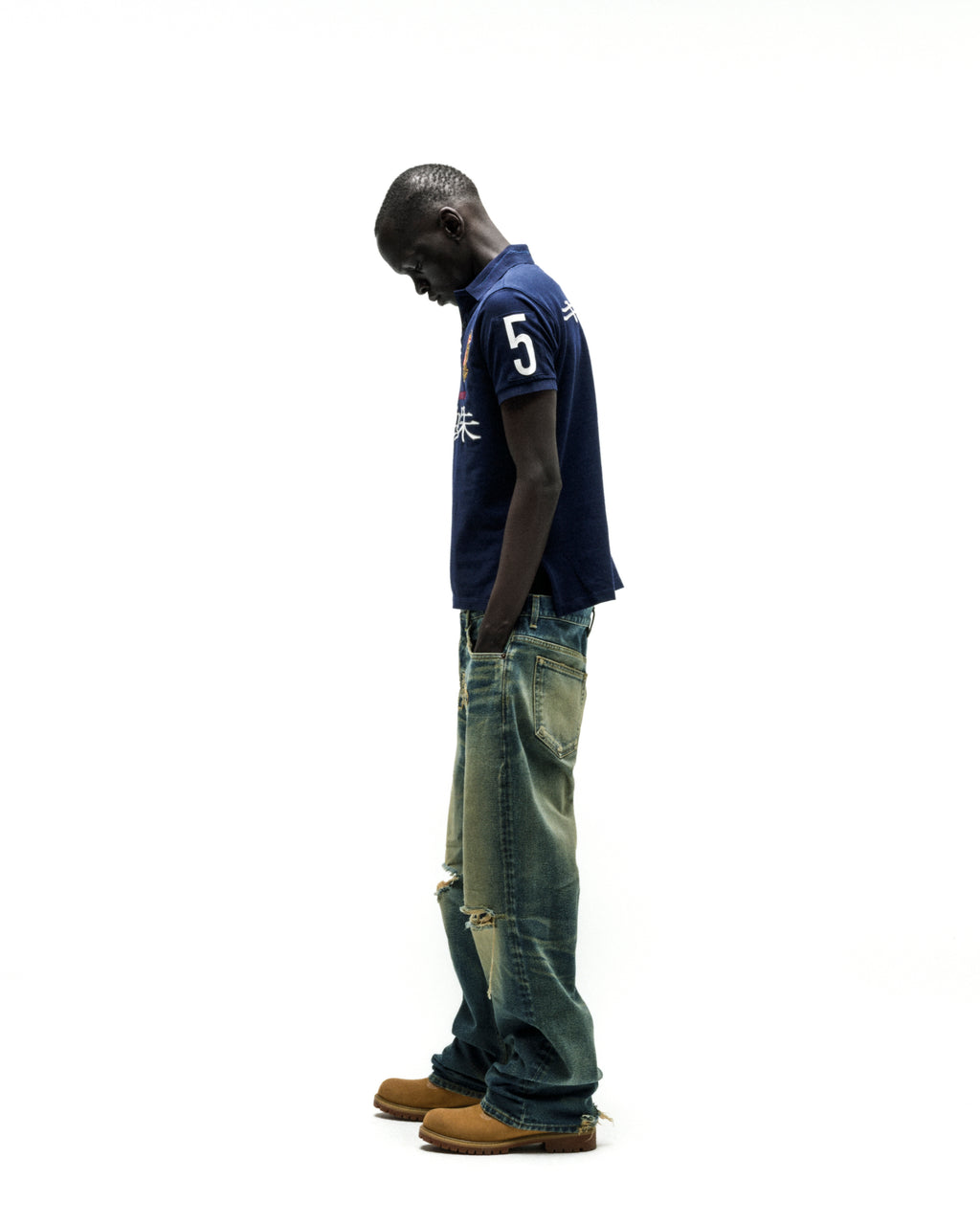 Dark blue polo shirt with "5" and Japanese text, paired with distressed wide-leg jeans and tan boots.