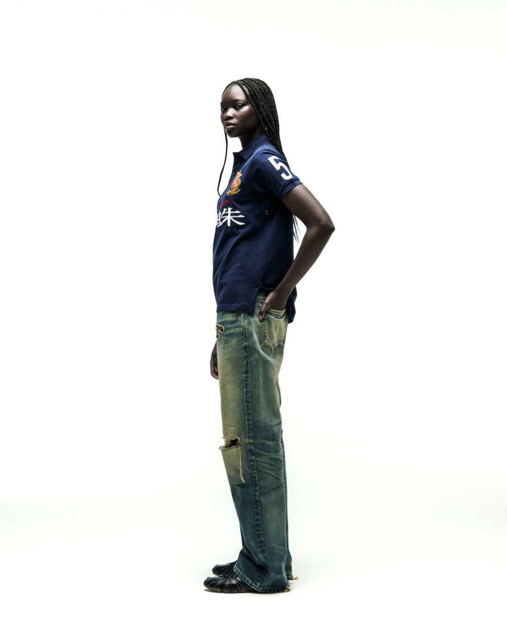 Dark-skinned model in a navy blue WORLDWIDE POLO shirt with white numbers and red text, paired with distressed jeans.