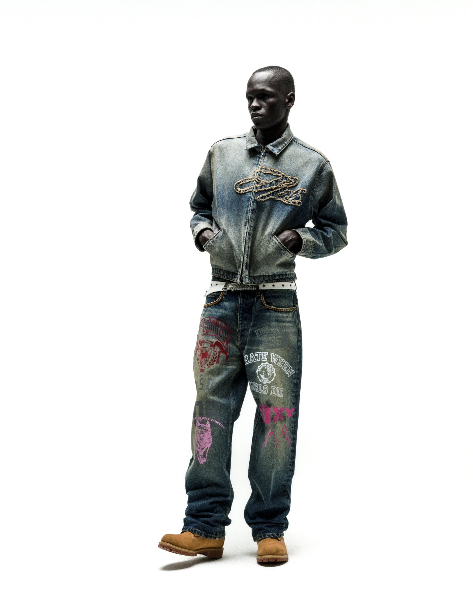 Worn-in blue denim work jacket with chain script embroidery, paired with graphic-printed jeans.
