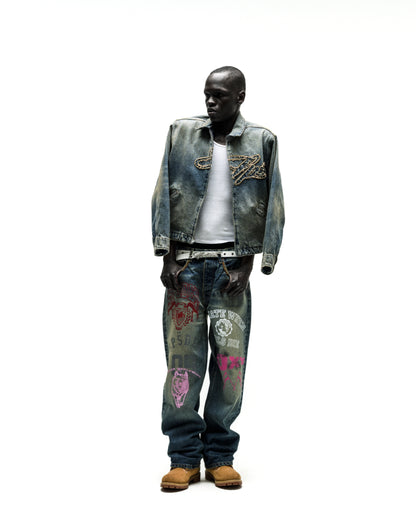 Worn blue denim work jacket with chain embroidery, paired with graphic jeans and a white tee.
