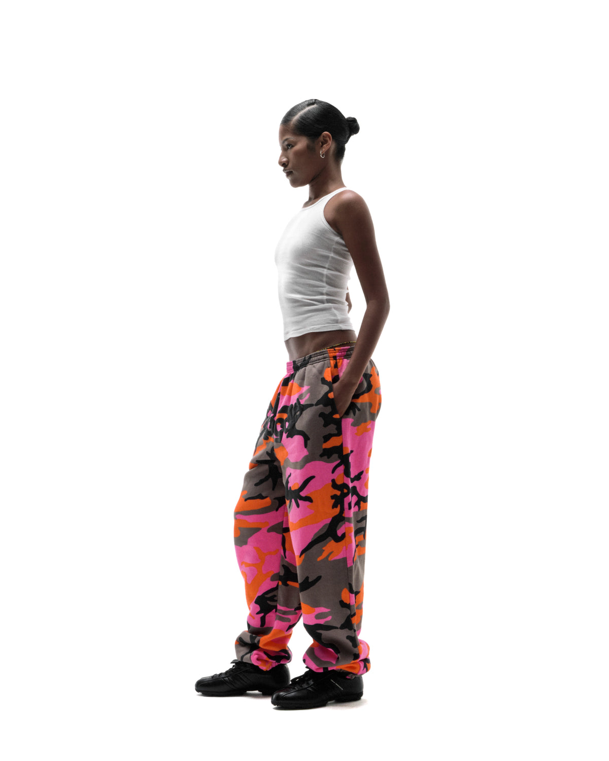 Model wearing a white ribbed tank top and vibrant pink and orange camouflage sweatpants against a white background.