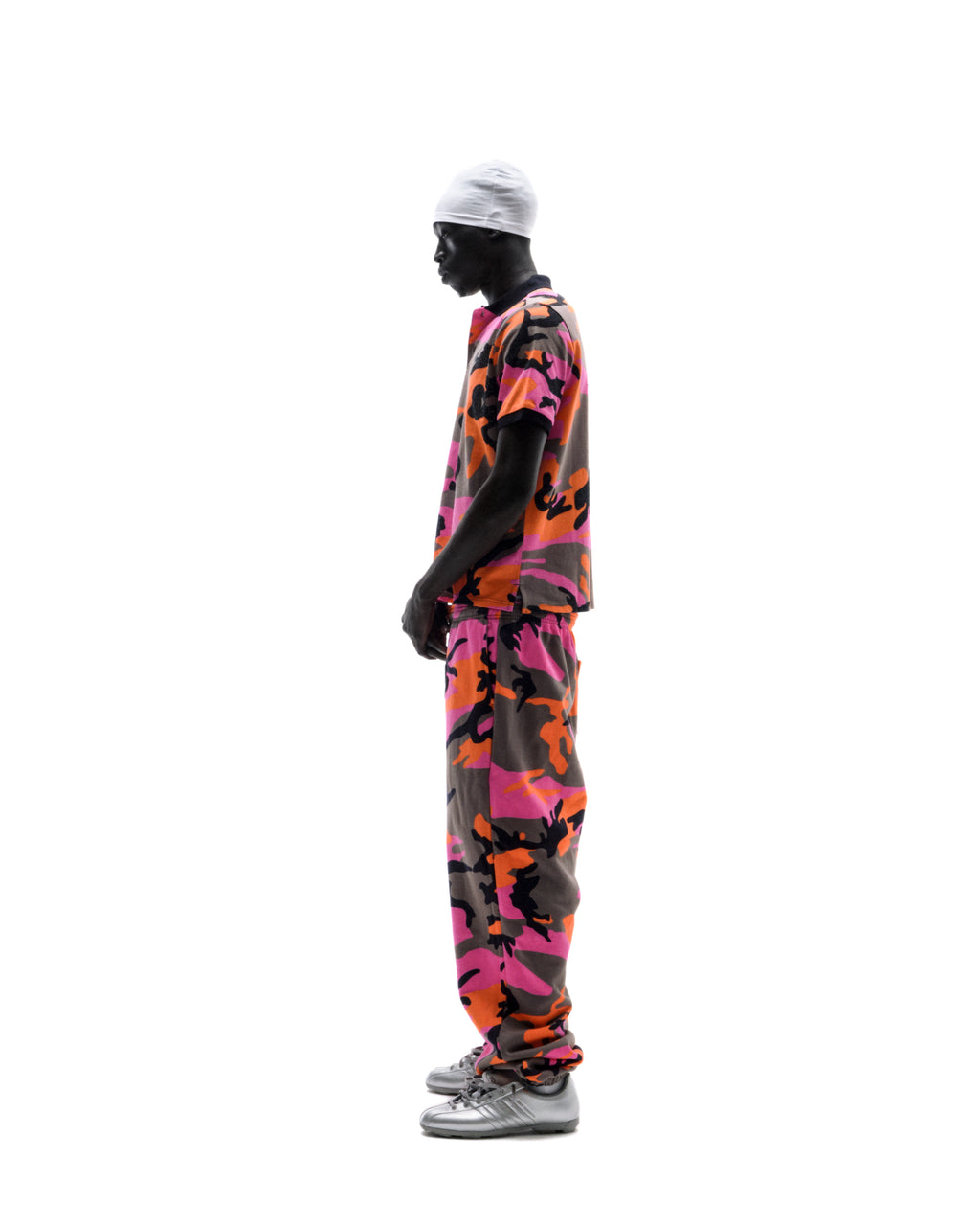 Model wearing a pink and orange camouflage polo shirt and matching joggers with a white beanie and silver sneakers.
