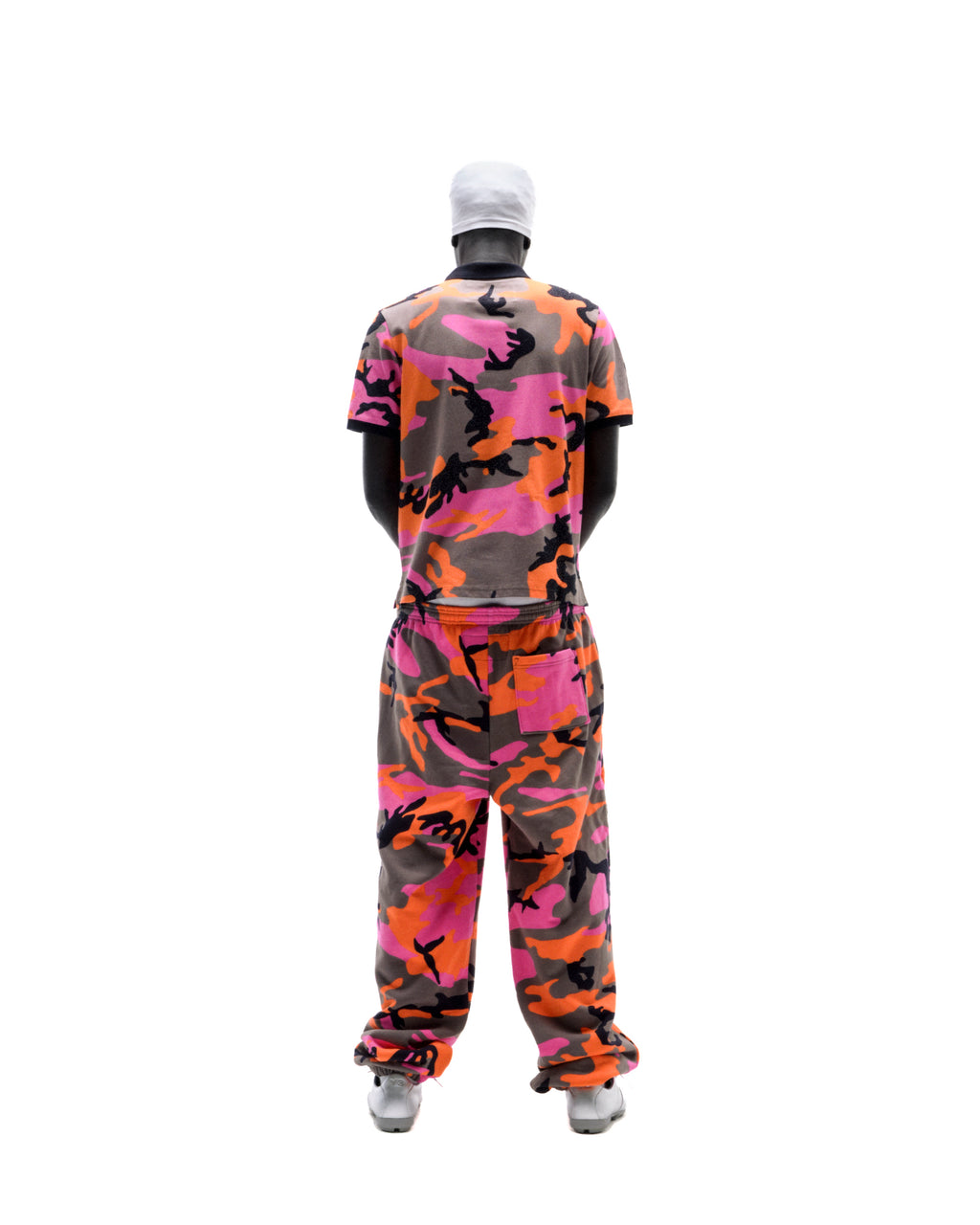 Model wearing a matching pink, orange, and grey camouflage t-shirt and sweatpants set with a white beanie.