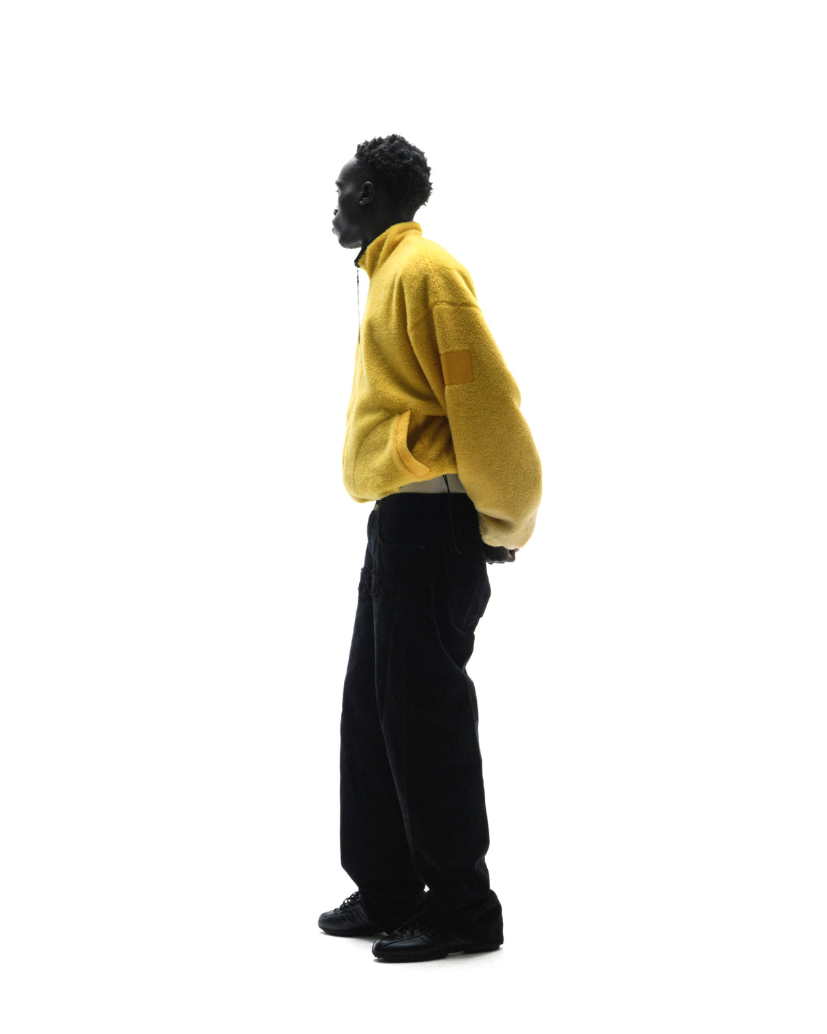 Model wearing a bright yellow fleece quarter-zip jacket and black trousers against a white background.