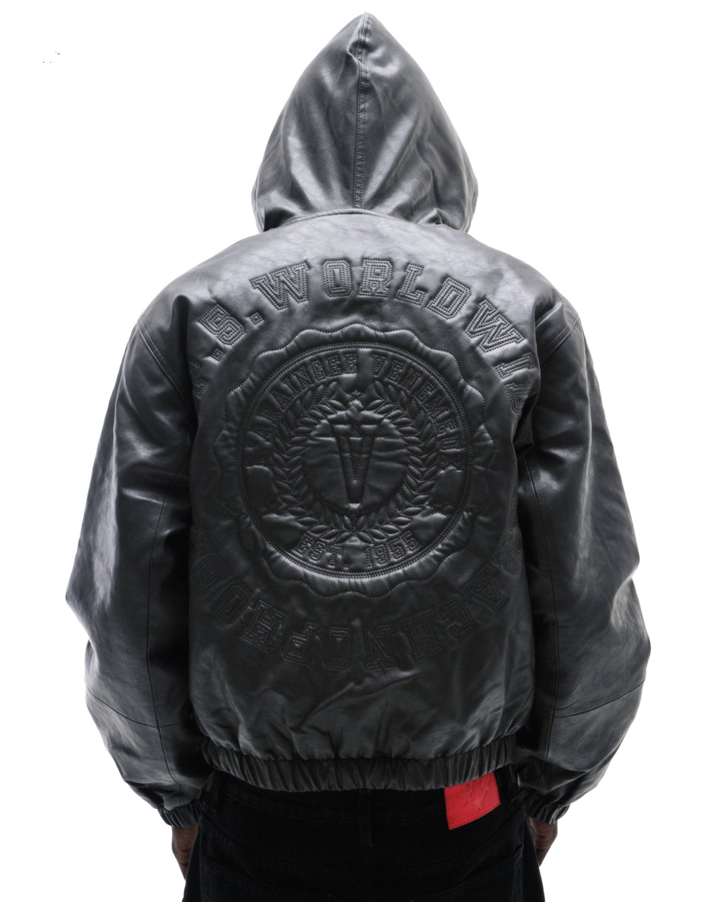Model wearing a black leather hooded bomber jacket featuring a large embossed circular logo on the back.