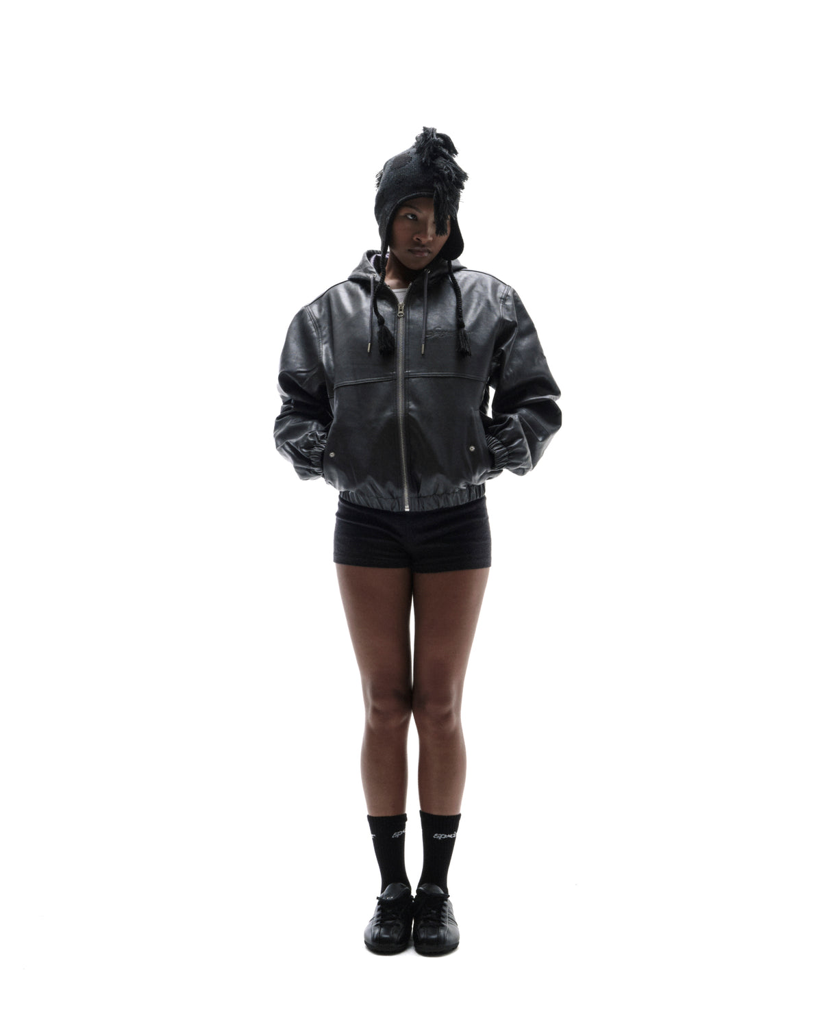 Model wearing a black leather bomber jacket, matching shorts, and a textured knit hat against a white background.