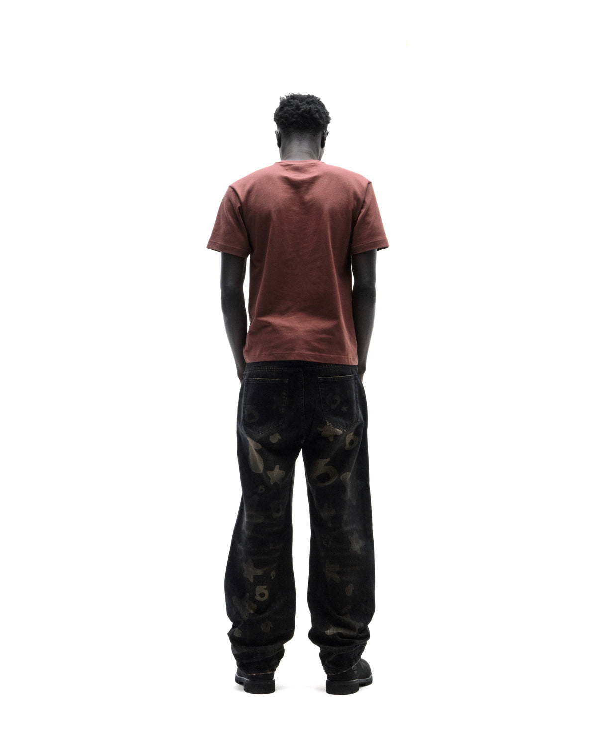 A model seen from behind wearing a plain brown t-shirt and loose-fit black denim jeans with a subtle star pattern.
