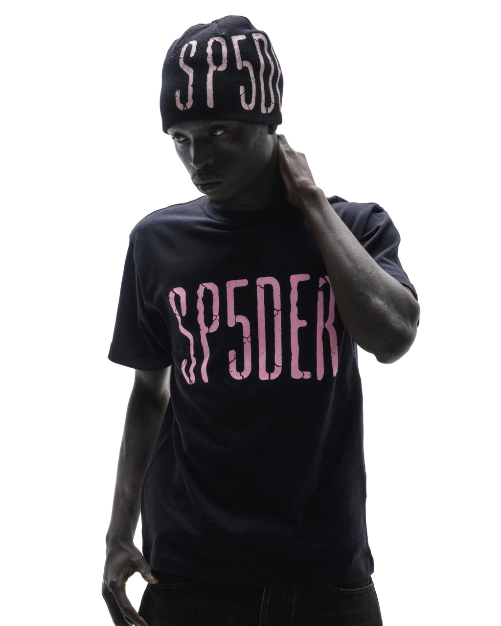 Model wearing a black SP5DER t-shirt and matching beanie with pink distressed lettering against a white background.