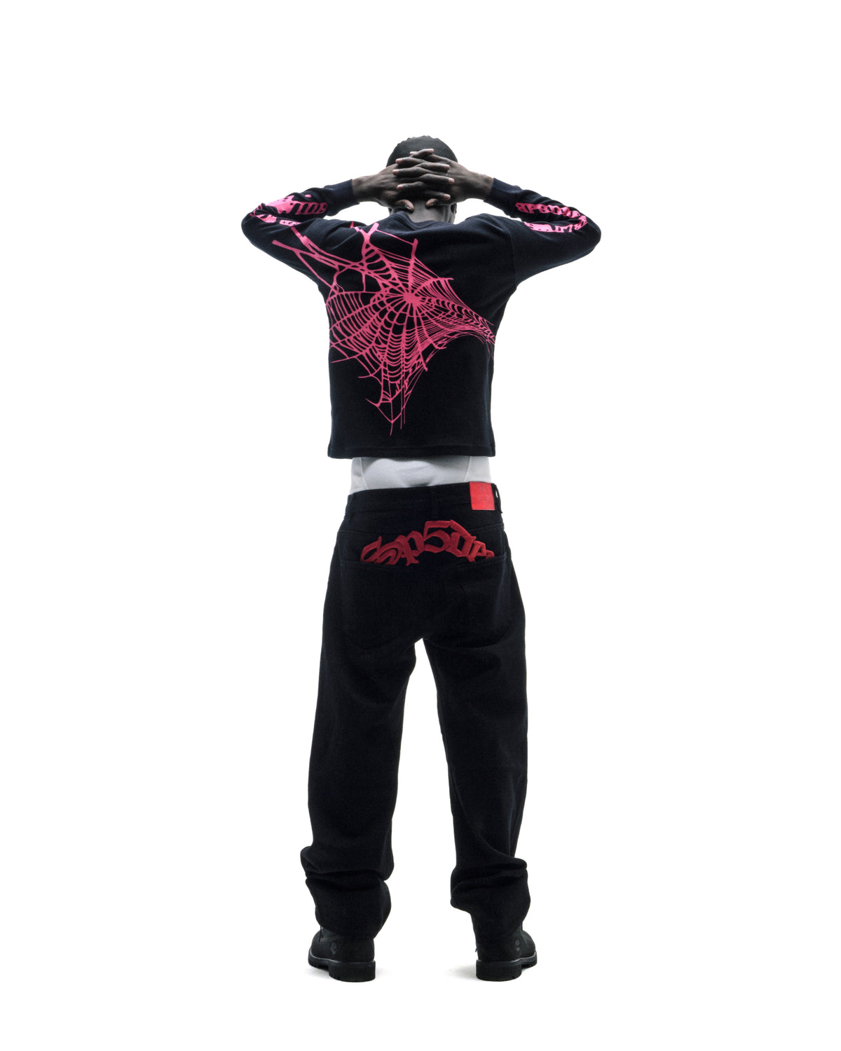 Model wearing a black long-sleeve shirt with pink spiderweb graphics and black jeans with red embroidered back pocket details.