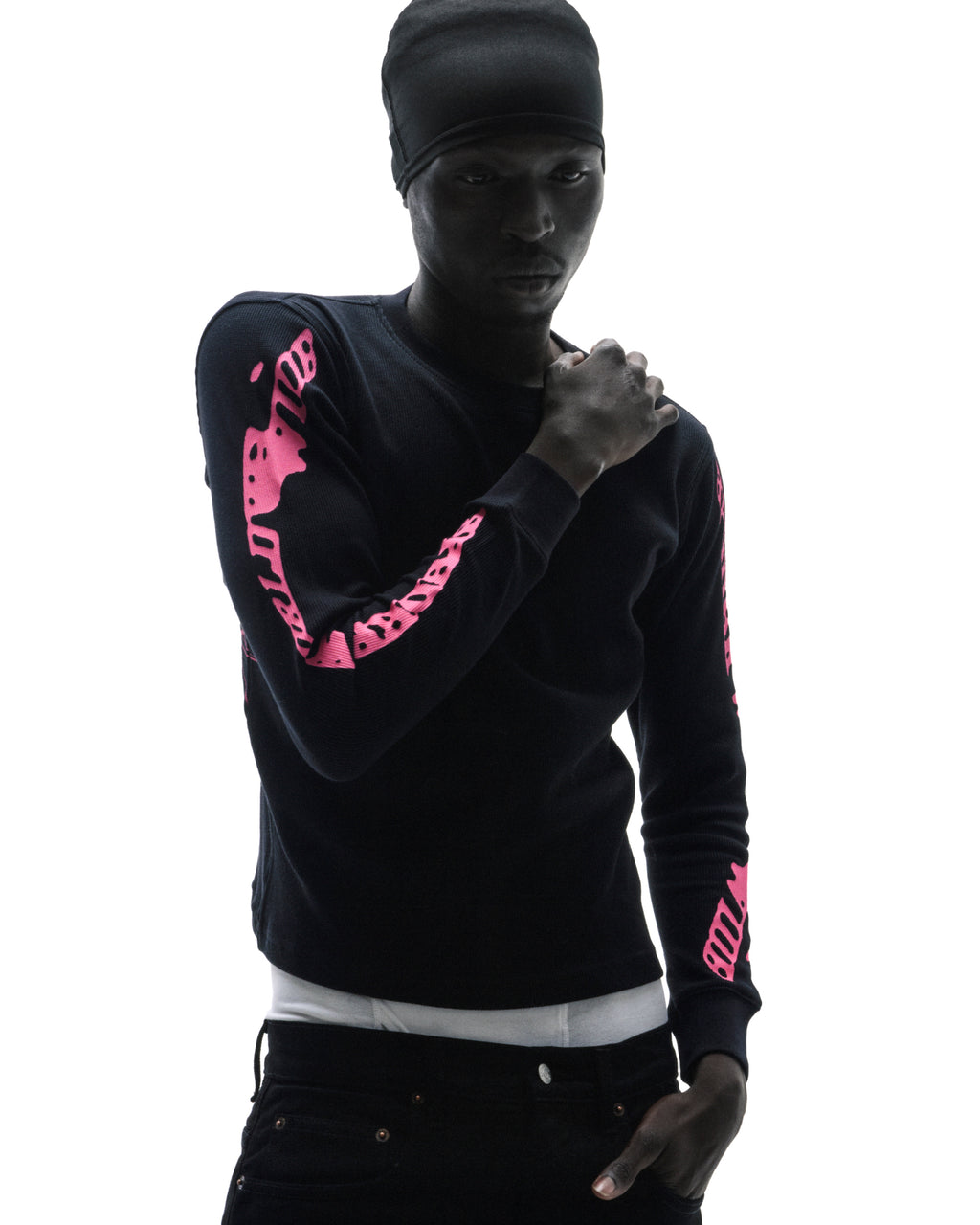 Model in a black long-sleeve thermal shirt with bright pink sleeve graphics and a black beanie against a white background.