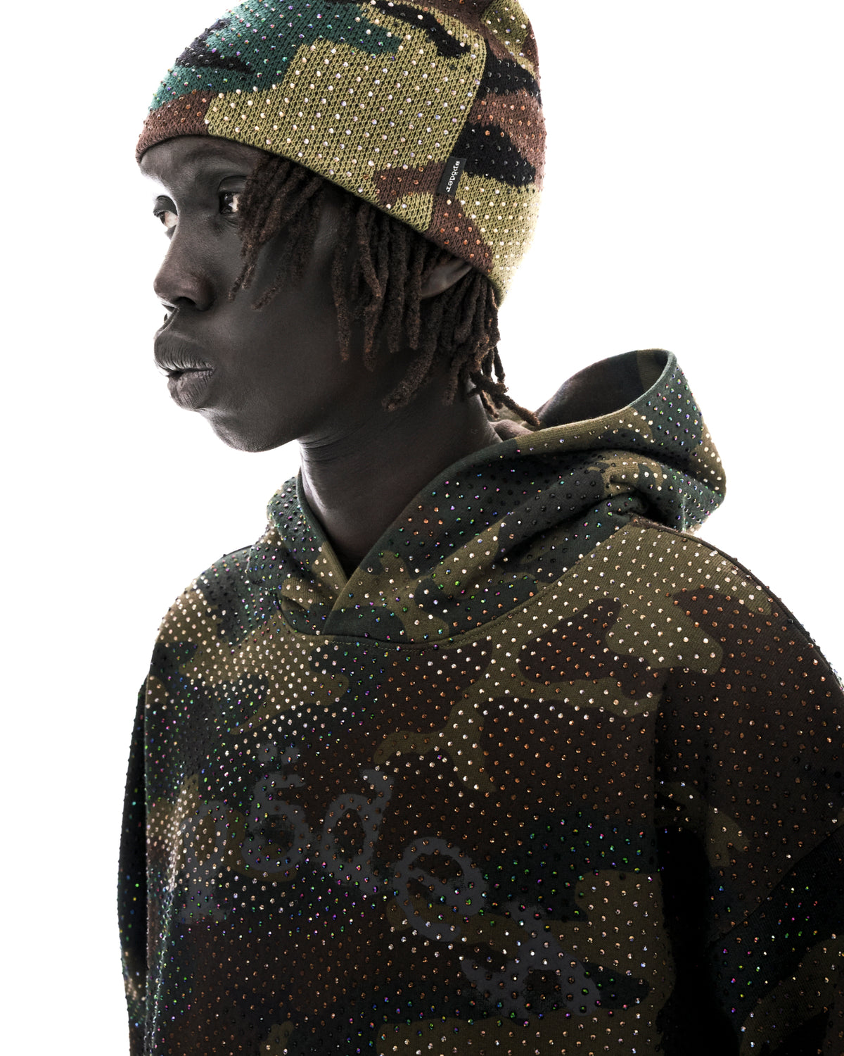 Model wearing a camouflage hoodie and matching beanie, both embellished with sparkling iridescent rhinestones.
