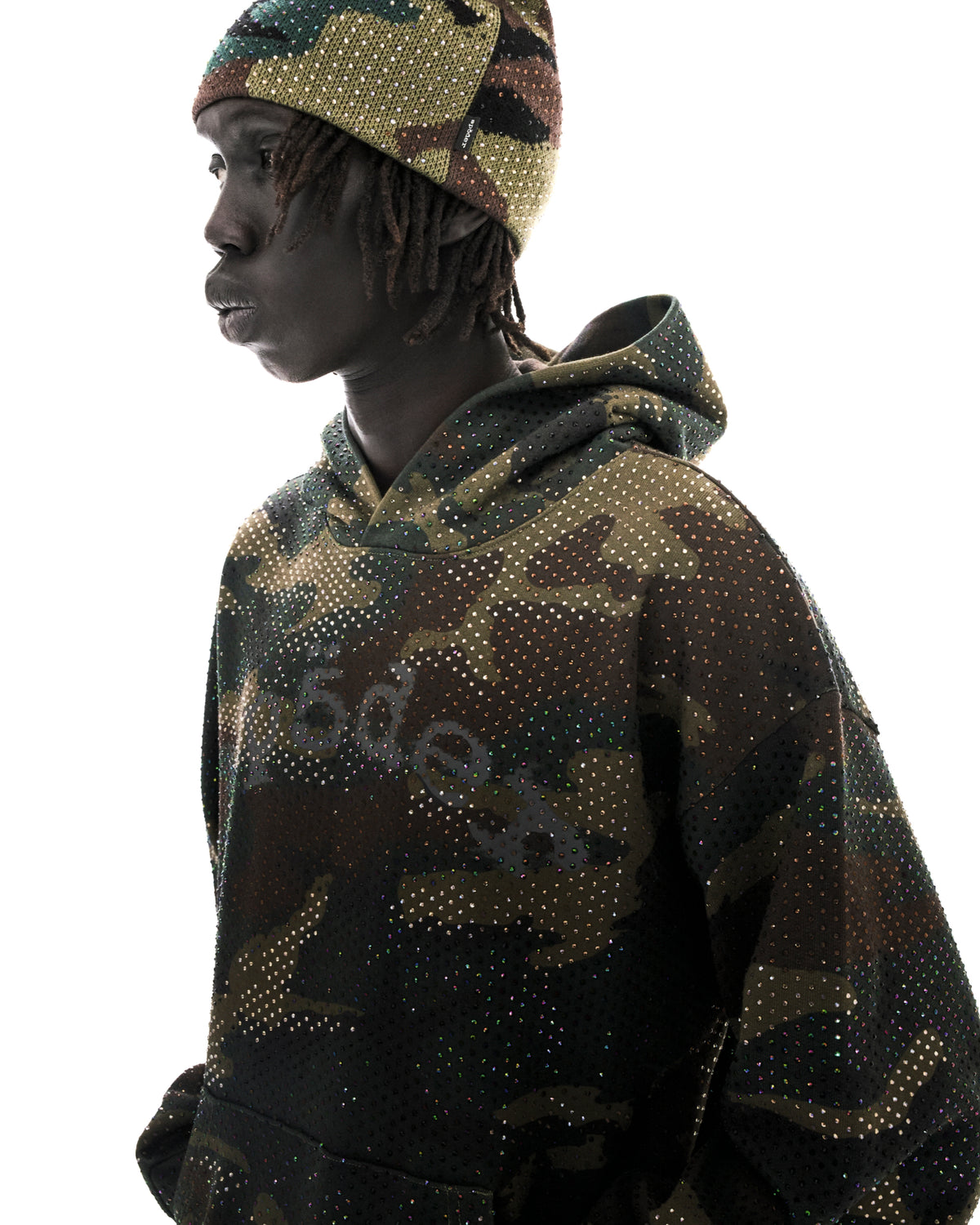 Model wearing a camouflage hoodie and matching beanie embellished with sparkling rhinestones against a white background.