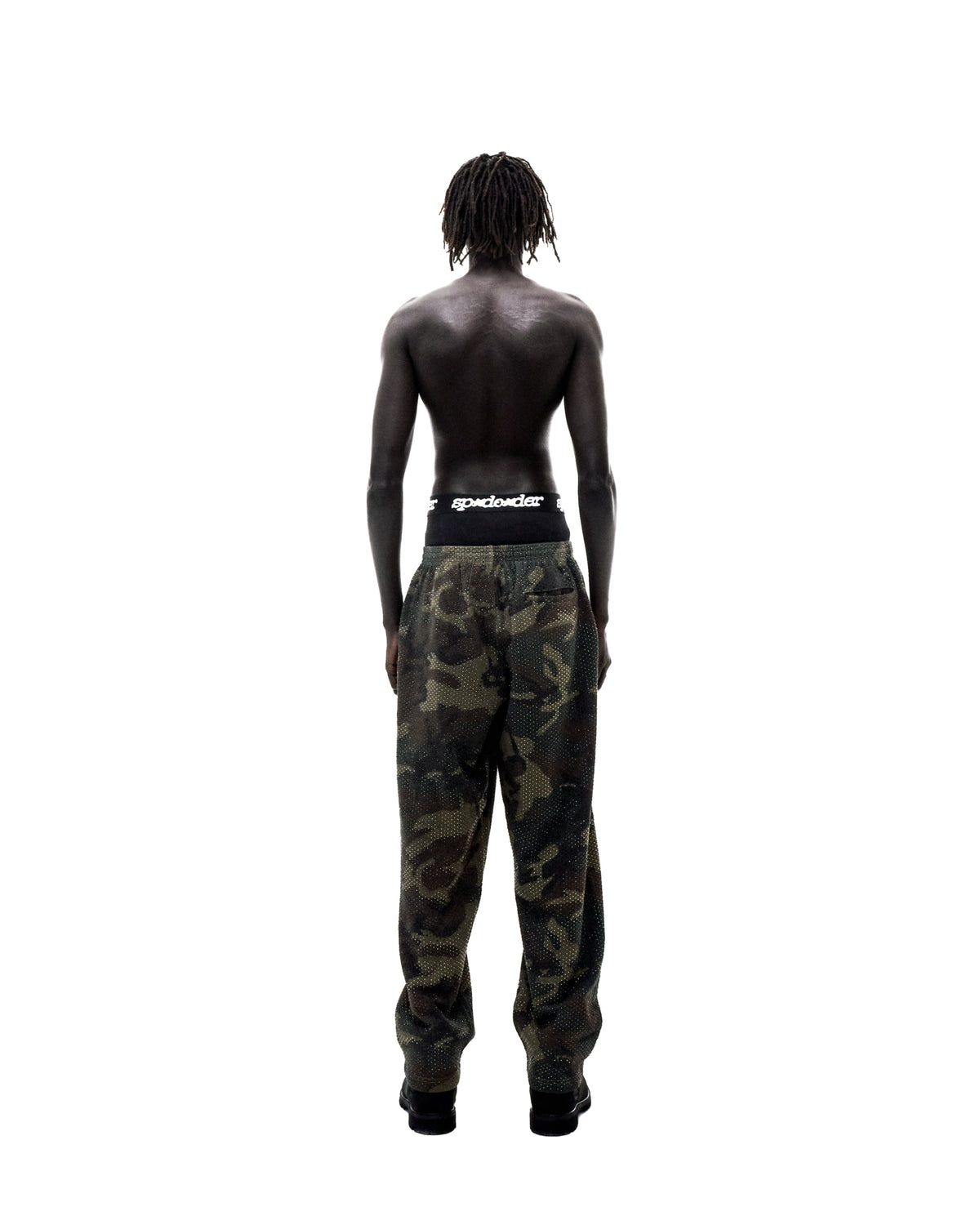 Shirtless model with dreadlocks wearing camouflage pants and black branded underwear, seen from behind.
