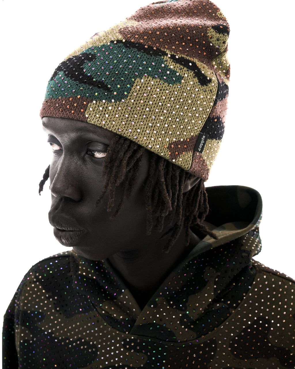 Model wearing a camouflage beanie and matching hoodie embellished with sparkling rhinestones against a white background.