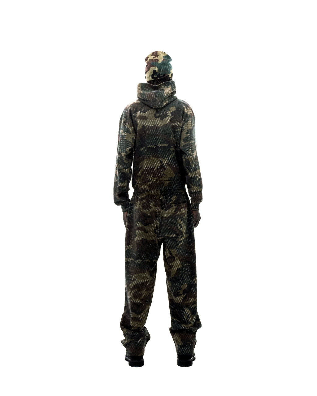 Model wearing a camouflage hoodie, matching pants, and a beanie, featuring a subtle dotted pattern on a white background.