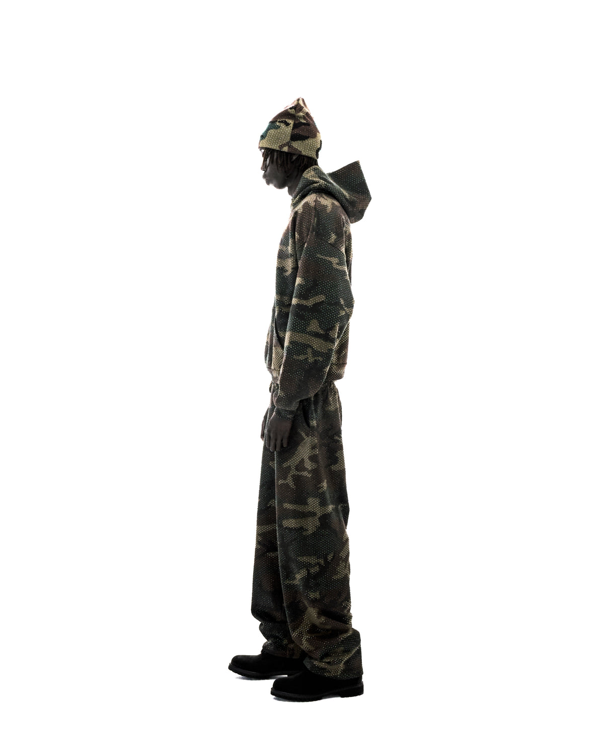 Model wearing a camouflage hoodie, matching pants, and beanie with a subtle dotted texture against a white background.