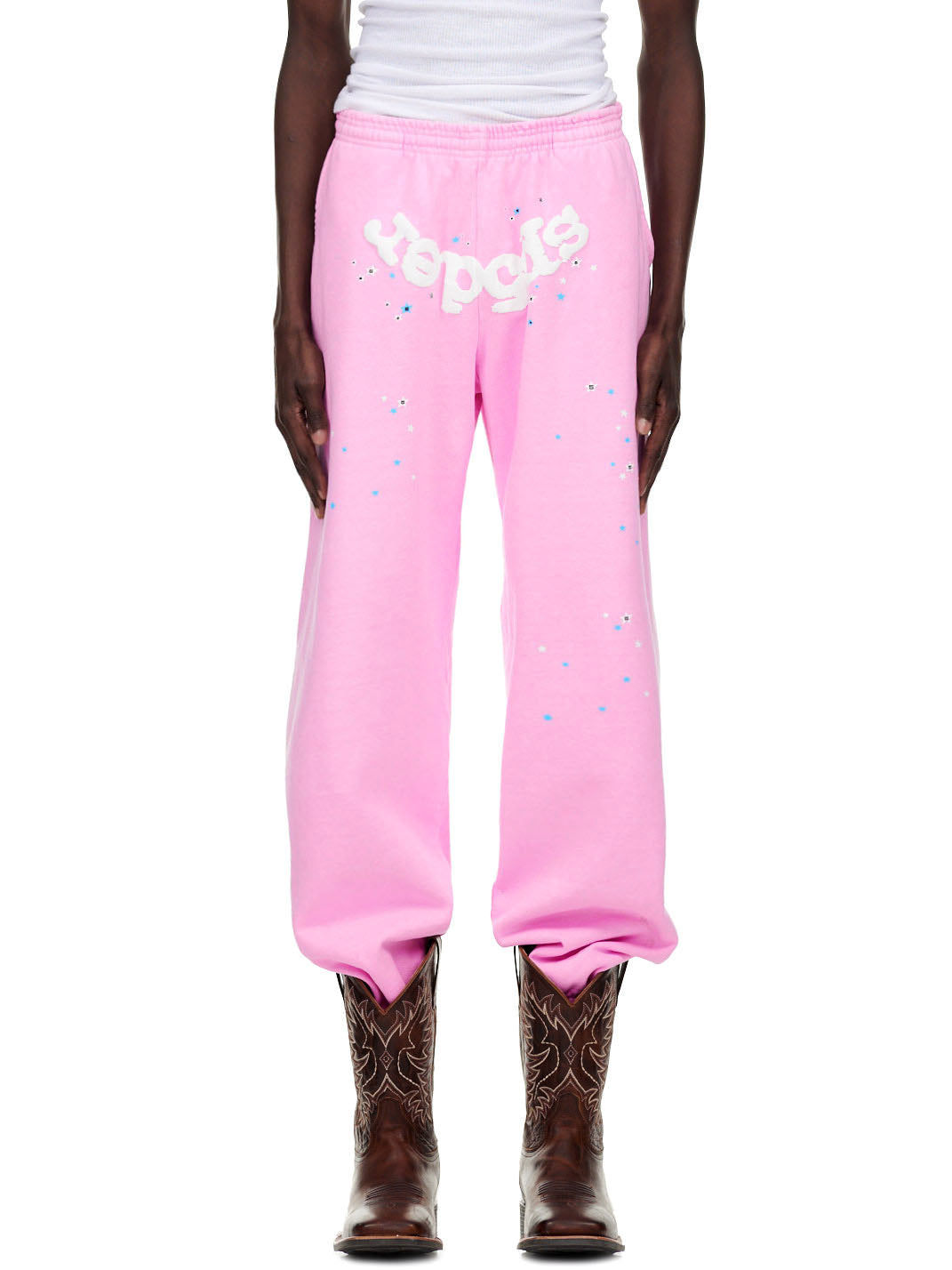 OG WEB PINK SWEATPANT with puff print "Spider" text and scattered star details, worn with cowboy boots.