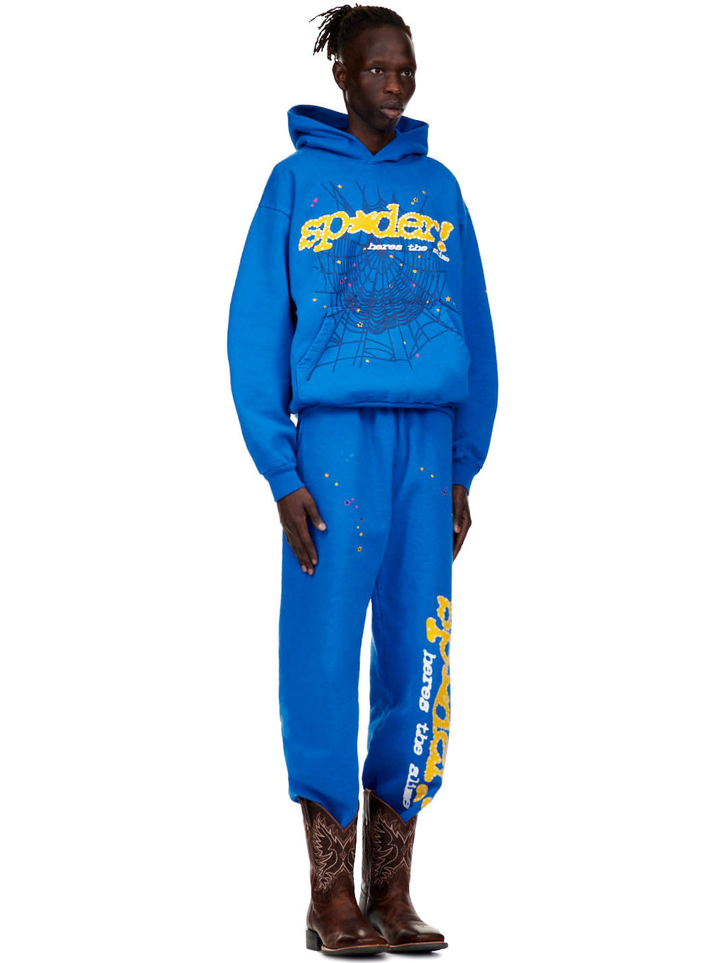 Male model in a blue fleece hoodie and sweatpants with "SP5DER!" text, star, and spiderweb prints.