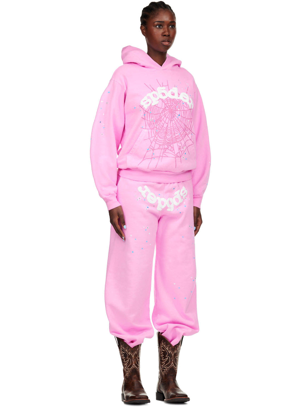 Female model in a pink OG WEB SP5DER sweatpant and matching hoodie with white puff print spiderweb and text.