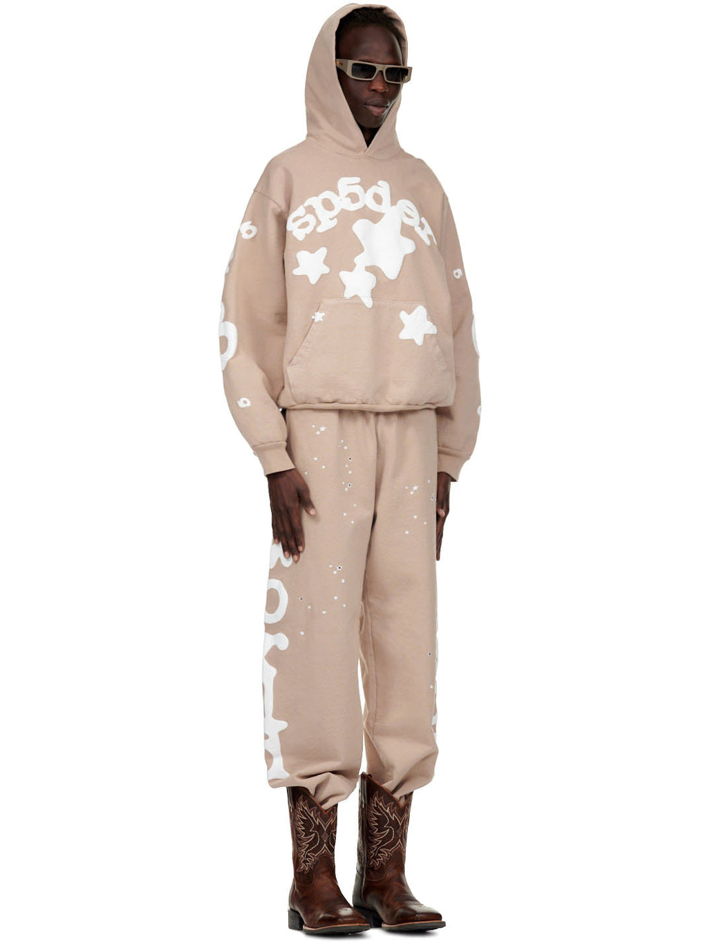 Male model in sand beluga sweatpant and matching hoodie with white puff print, stars, and worldwide text.